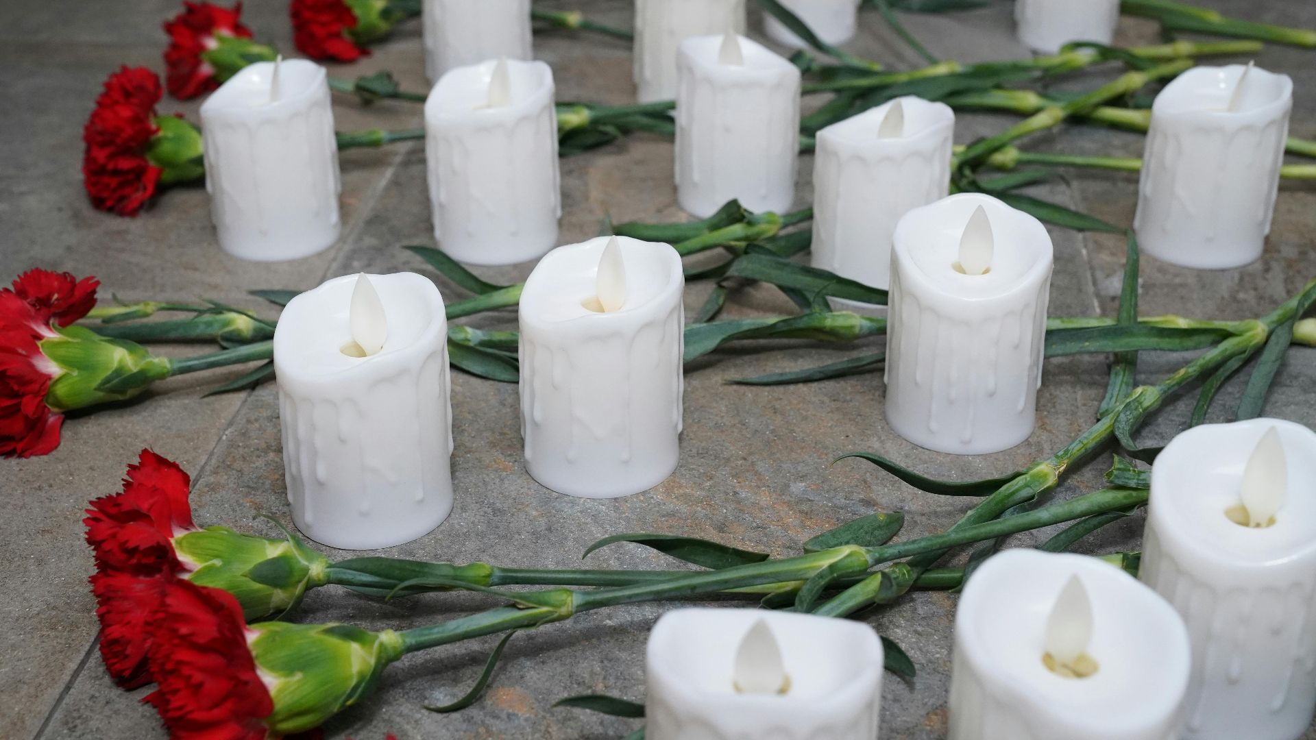 Red carnations and white candles arranged on the floor for a memorial setup.