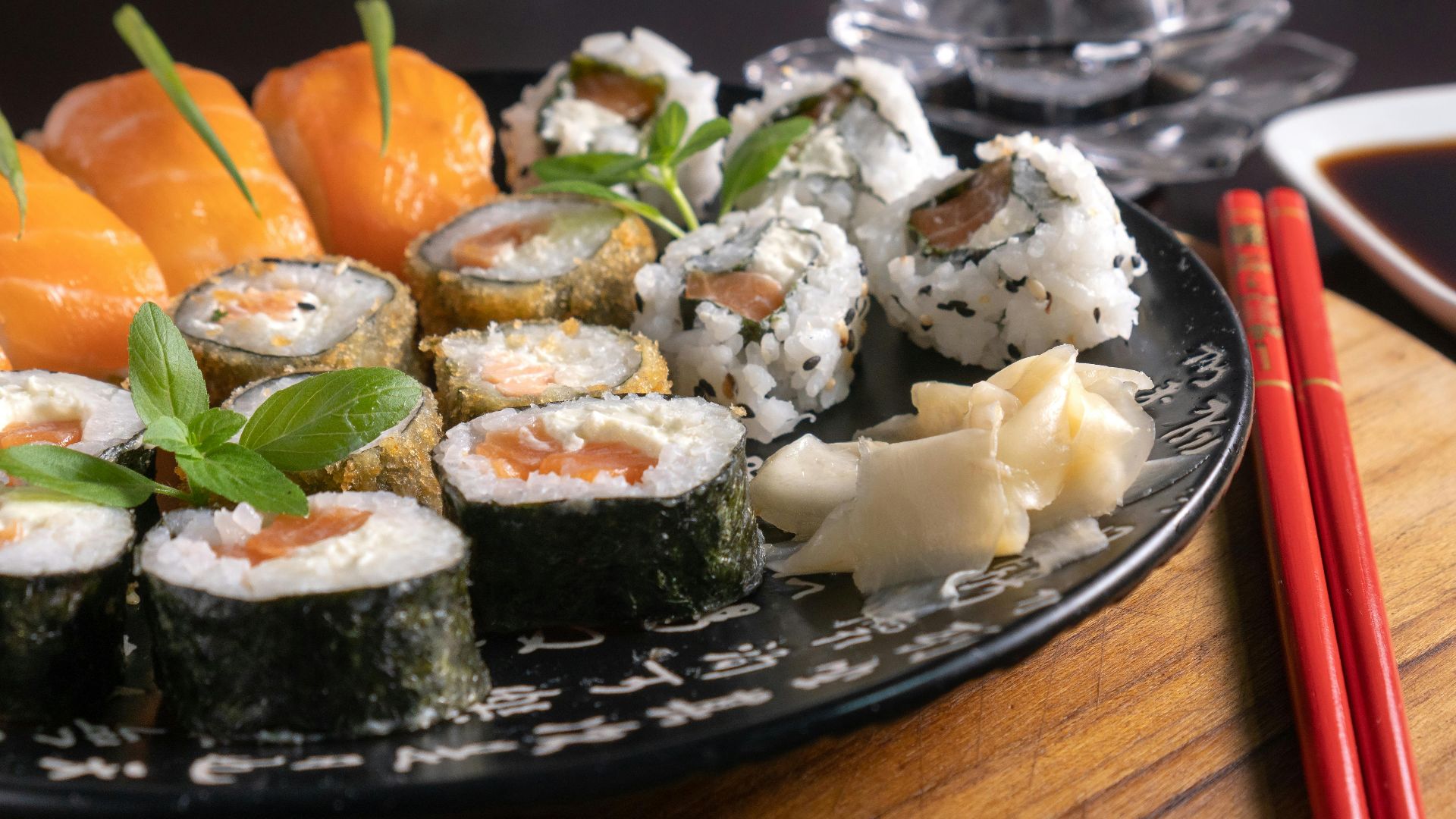 A mouth-watering assortment of sushi served with soy sauce, garnished with fresh herbs, and chopsticks on a wooden board.