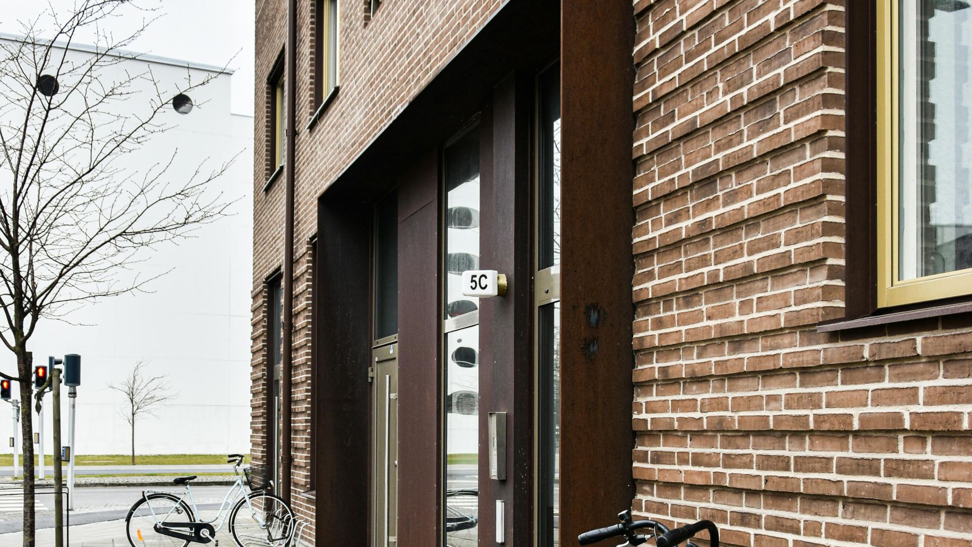 Sidewalk view of a brown brick building with bicycles. Modern urban environment.