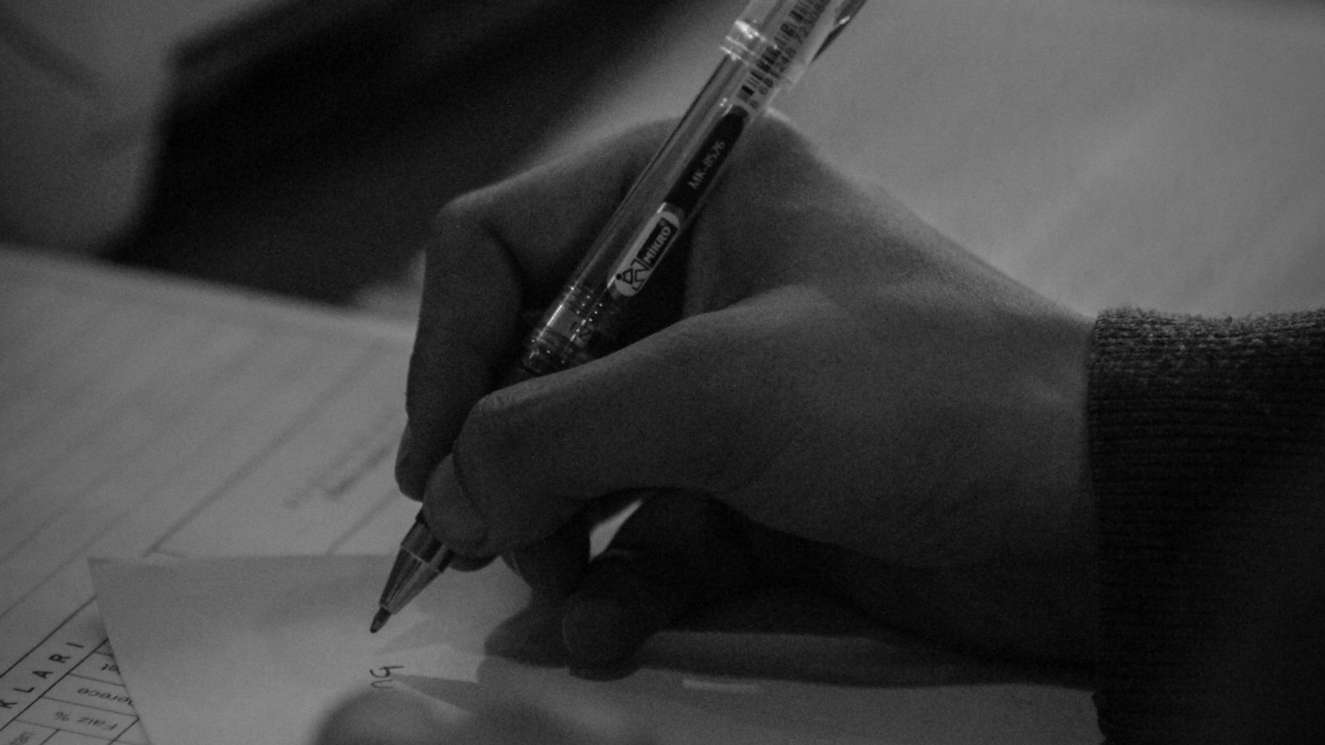 Black and white shot of hands writing with a pen on paper, conveying focus.