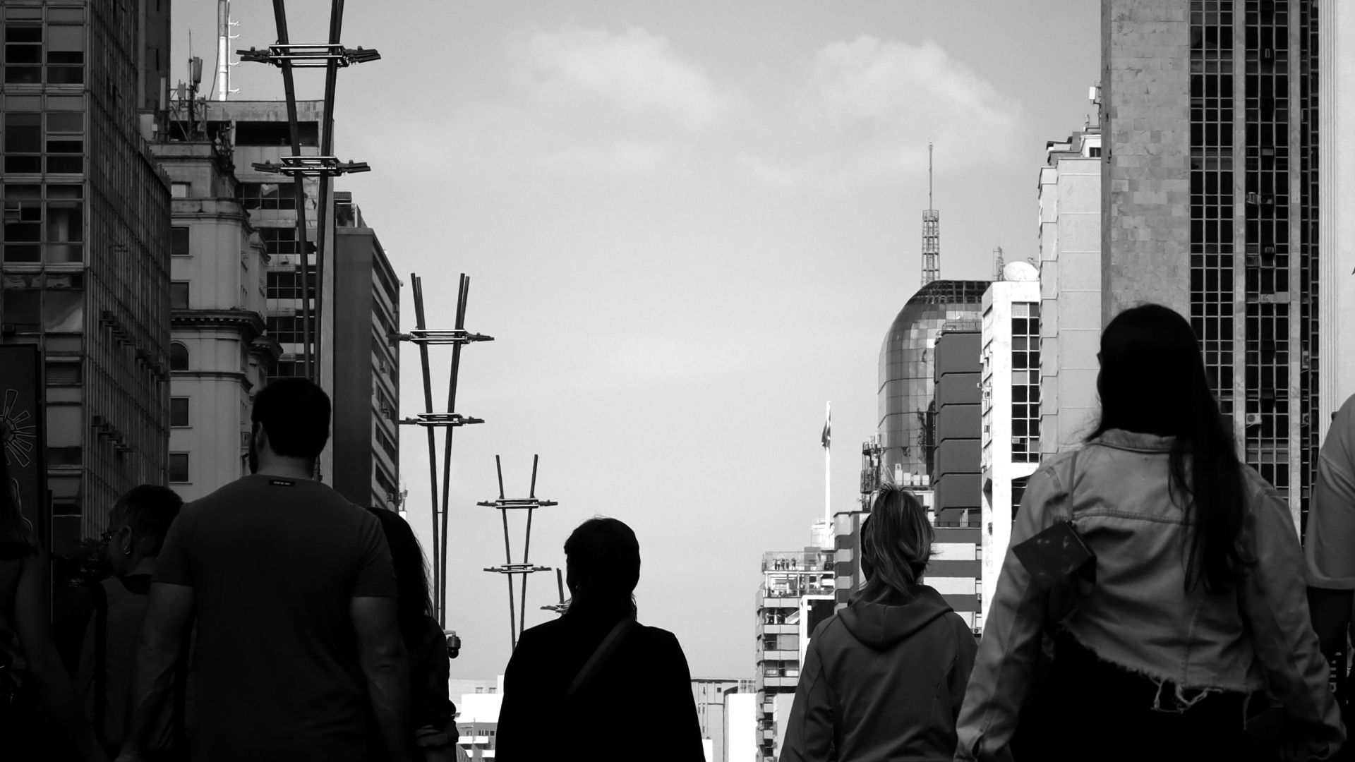 Black and white photo of people walking in a bustling city street lined with tall buildings.