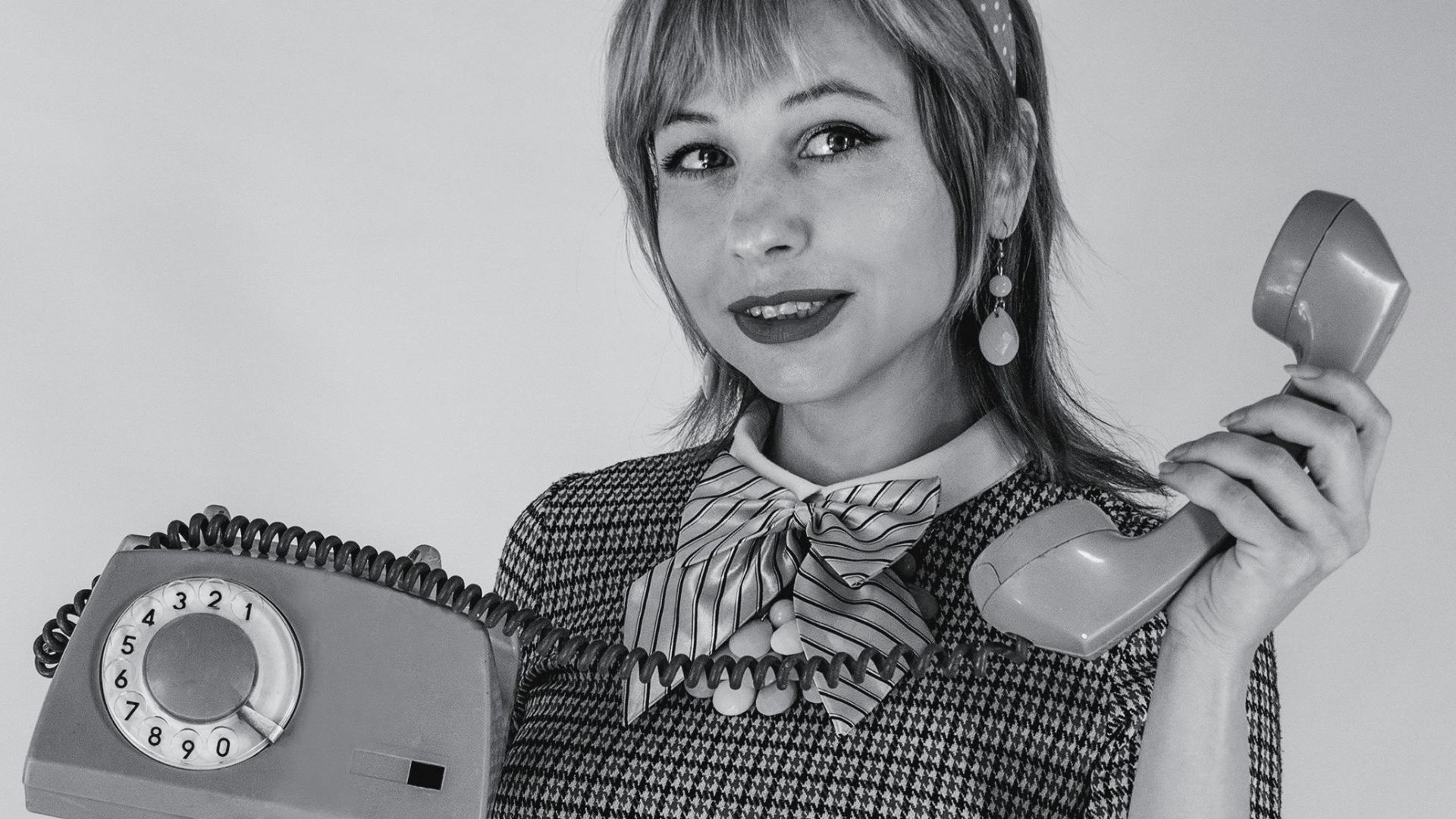 Caucasian woman in vintage attire holding a rotary phone, studio black and white.