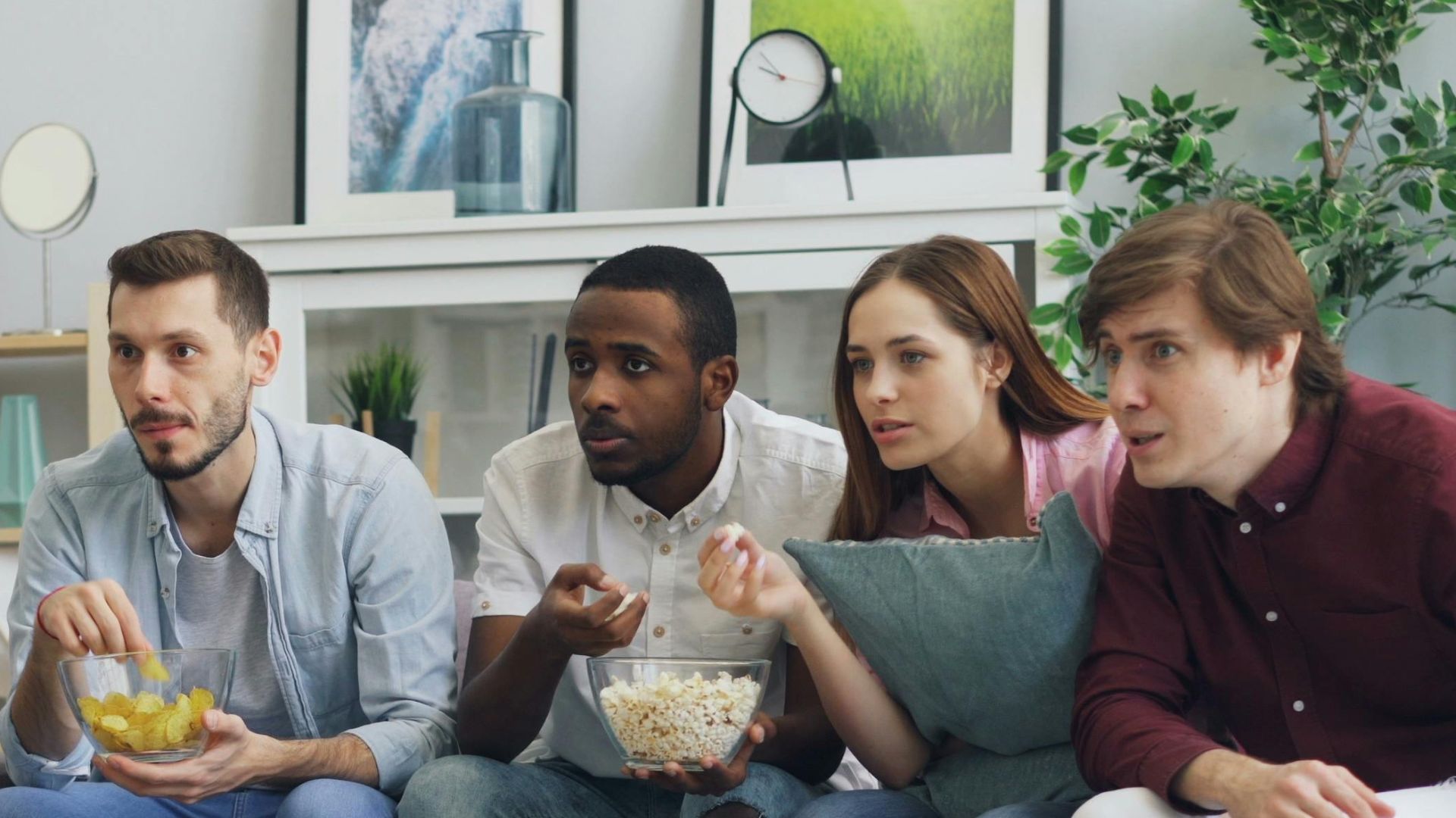 Group of friends watching a thriller movie at home, sharing snacks and reactions.
