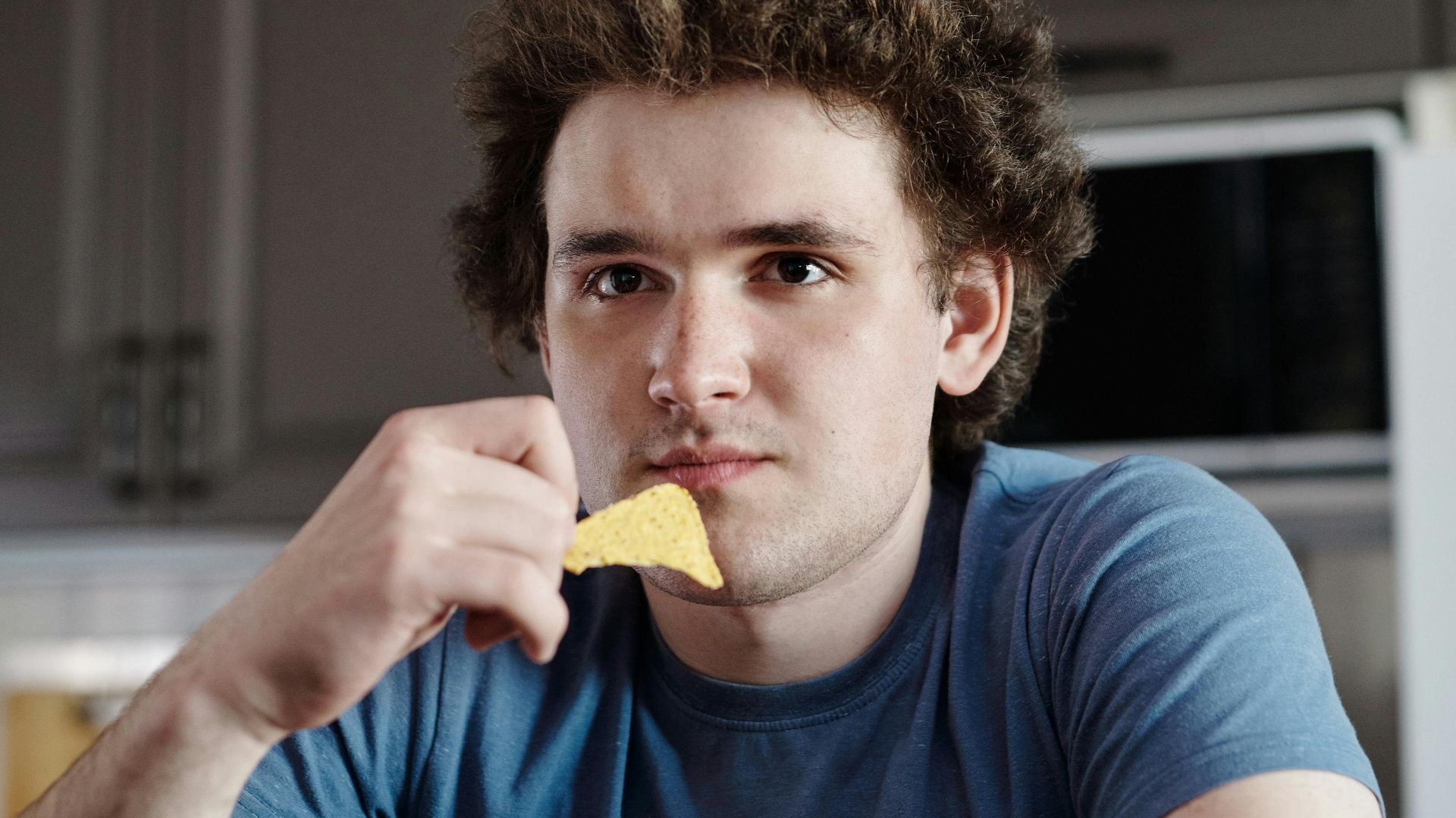Man enjoying nachos snack in kitchen setting, indoor casual scene.
