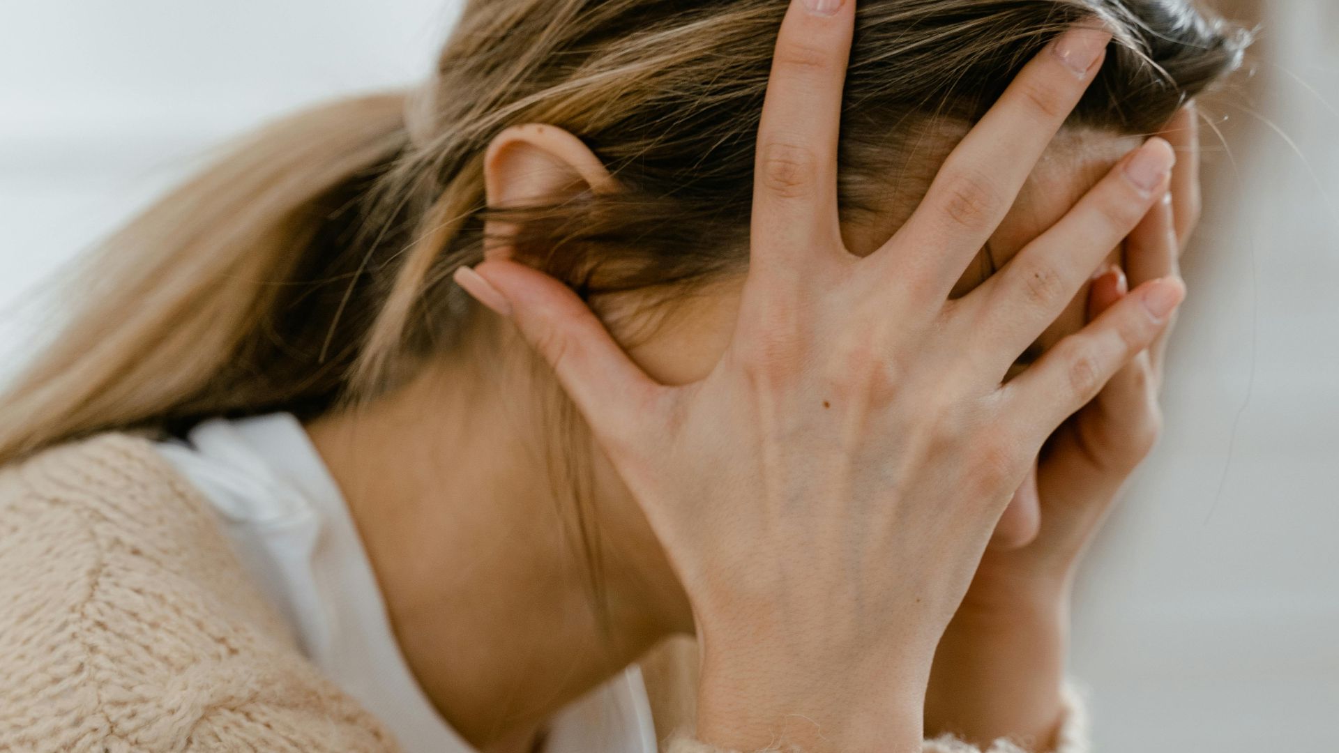 Woman sitting indoors with face covered by hands, expressing stress and frustration.