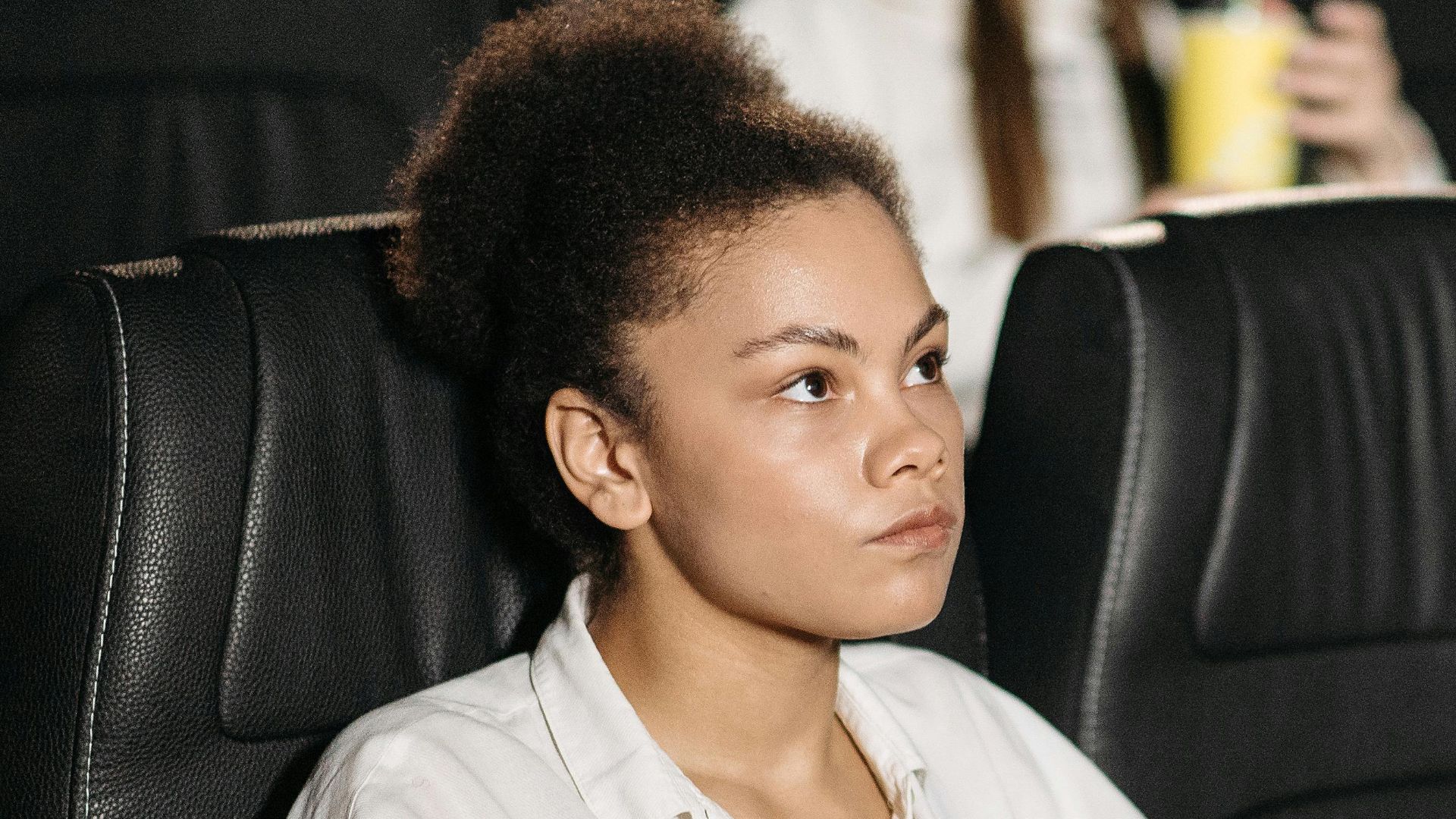 A woman sits in a movie theater holding popcorn, intently watching the screen.