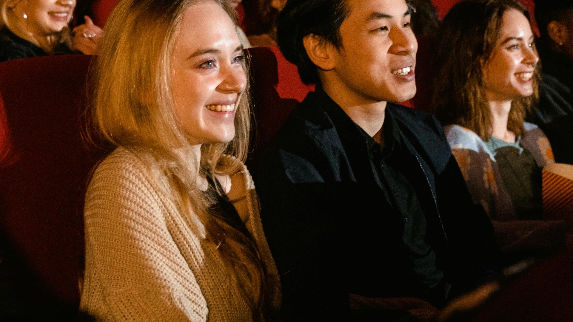 A diverse group of friends enjoying a movie at the cinema, with smiles and popcorn.