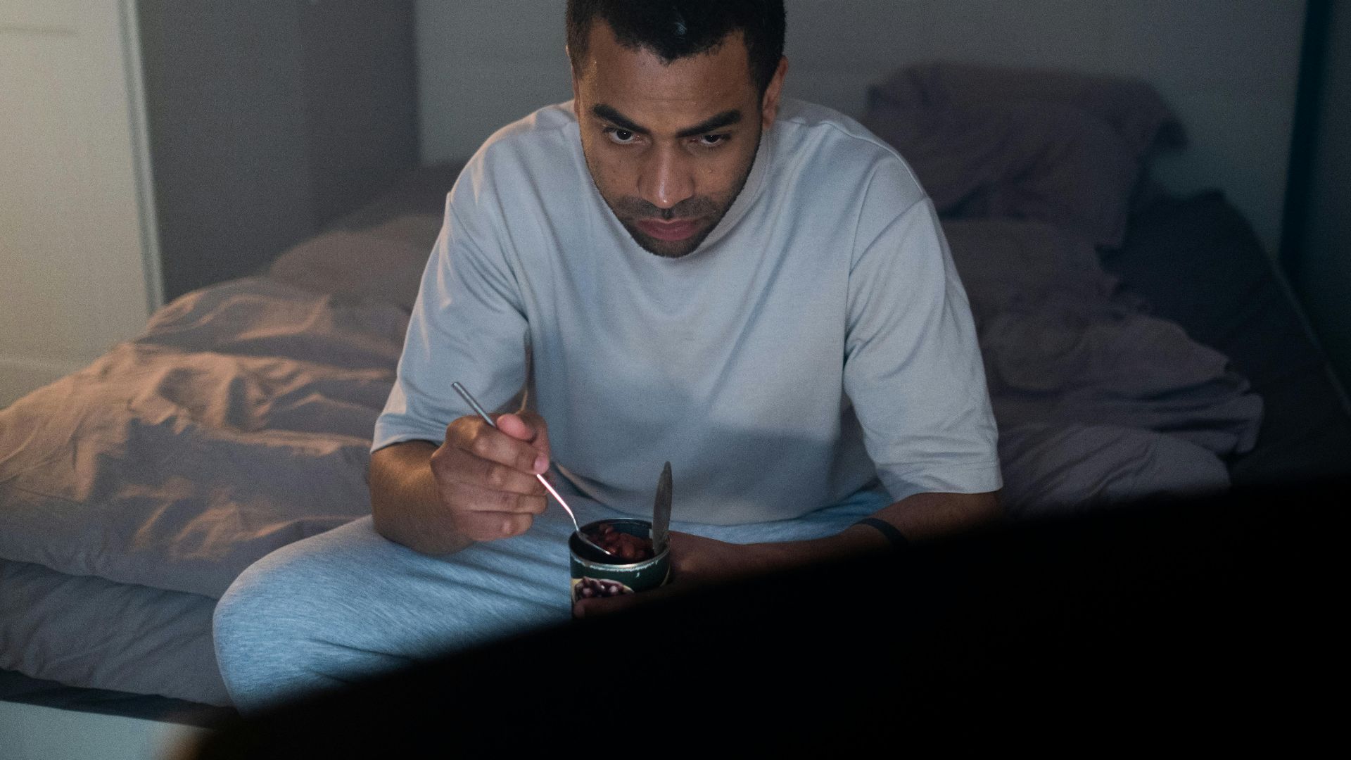 Adult male enjoying a dessert watching TV in a cozy bedroom setting.