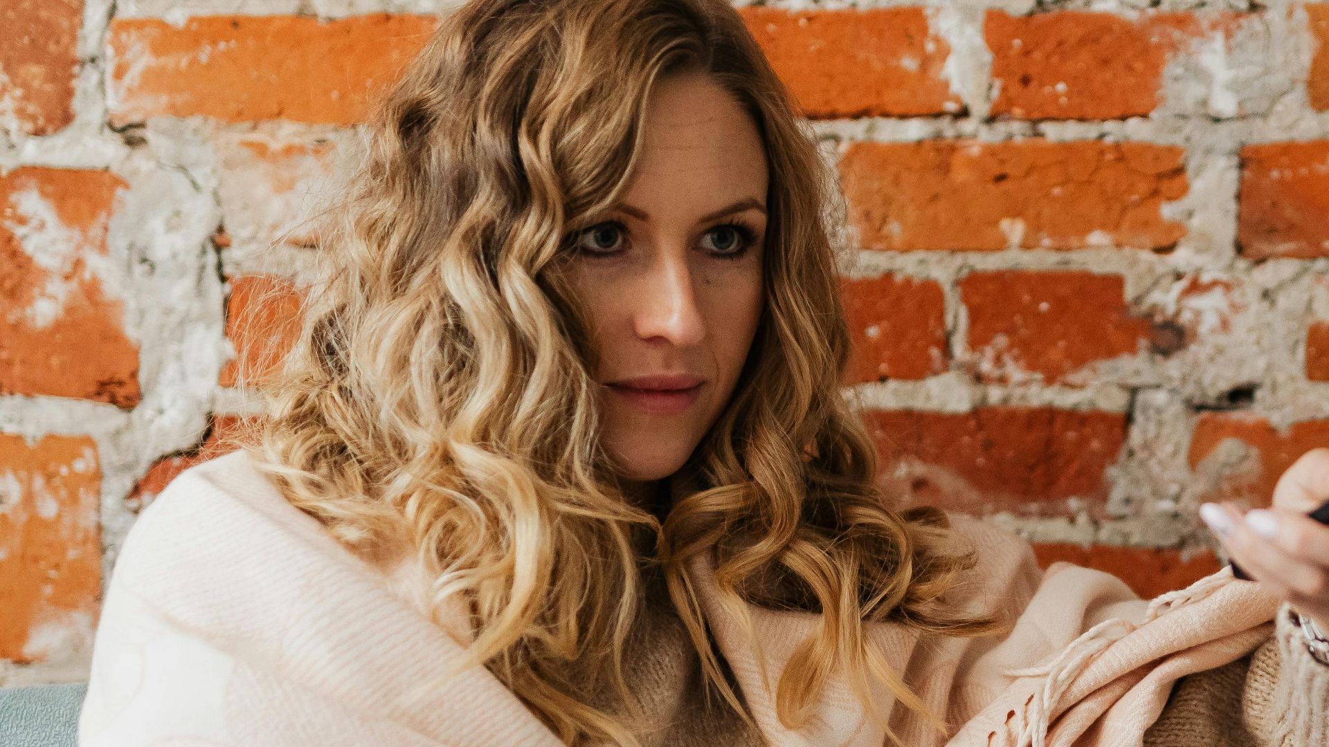 A woman wrapped in a blanket holding a remote control while sitting on a sofa indoors.
