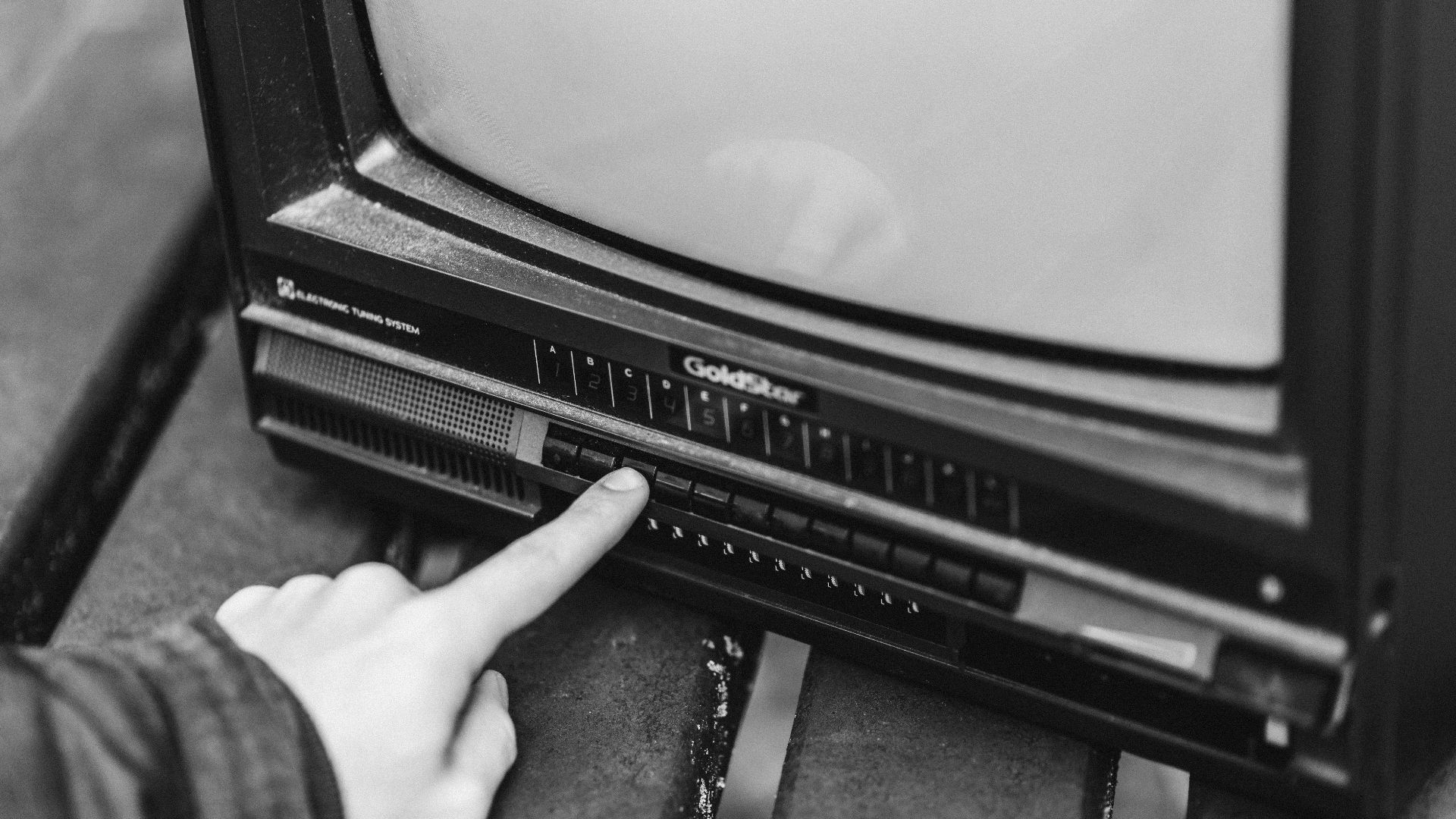 Black and white from above of anonymous male switching channels on retro black television placed in wooden table on street