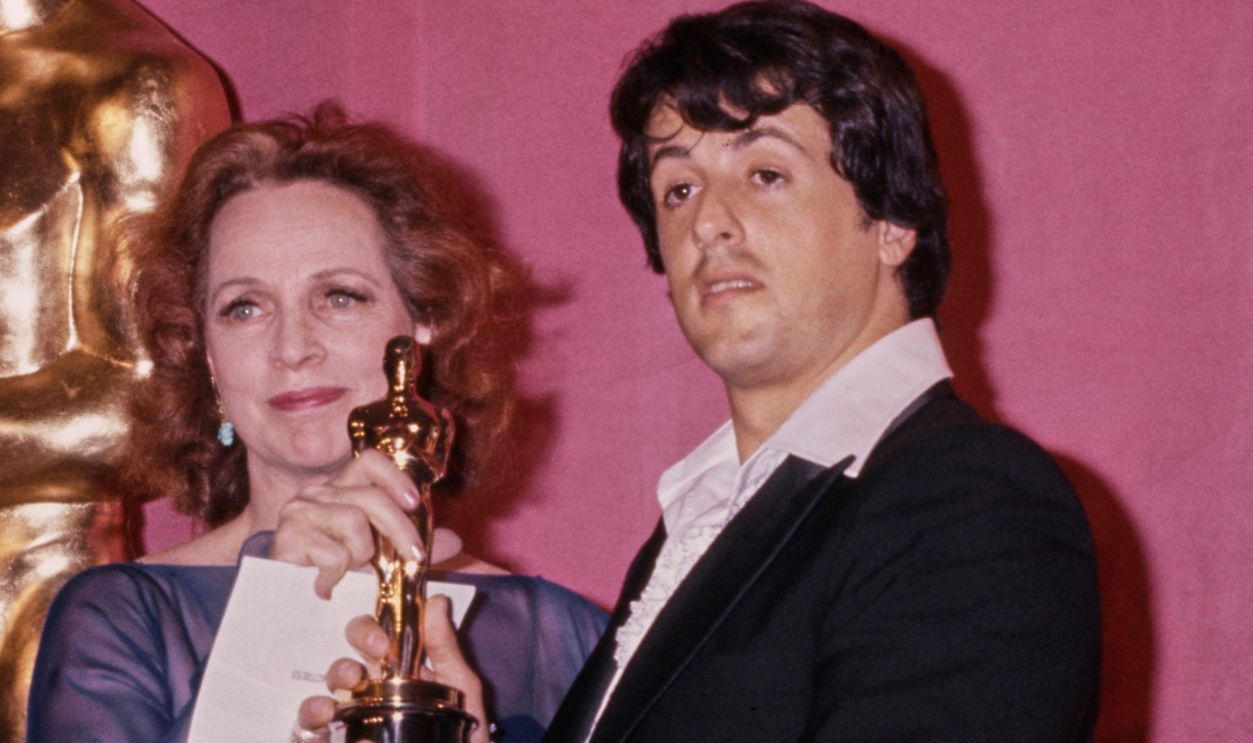 Getty Images - 2188163639 - American actress Beatrice Straight, wearing a blue dress, and American actor Sylvester Stallone, who wears a tuxedo over a white ruffled shirt, open at the collar, in the 49th Academy Awards press room, at the Dorothy Chandler Pavilion in Los Angeles, California, 28th March 1977. Straight holds her 'Best Supporting Actress' award (received for her performance in 'Network'), presented by Stallone who was nominated for two awards ('Best Original Screenplay' and 'Best Actor', both for 'Rocky') at the ceremony.