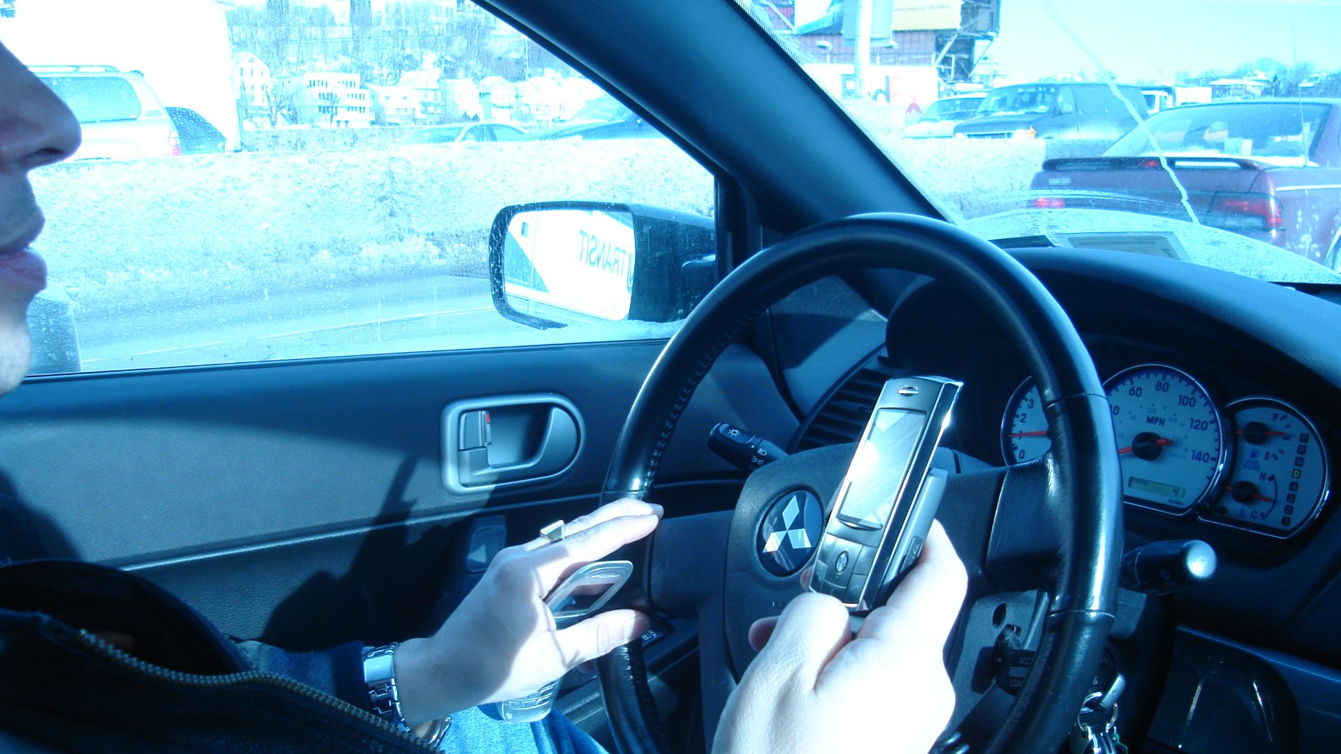 New York driver in a Mitsubishi Galant using two hand held mobile phones at once, in a traffic jam.