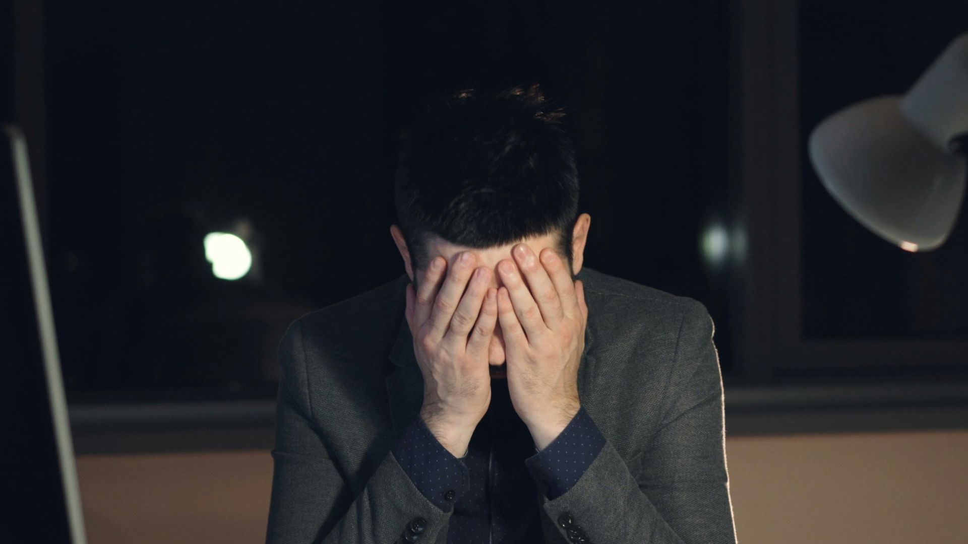 Man in suit sits at desk, head in hands.