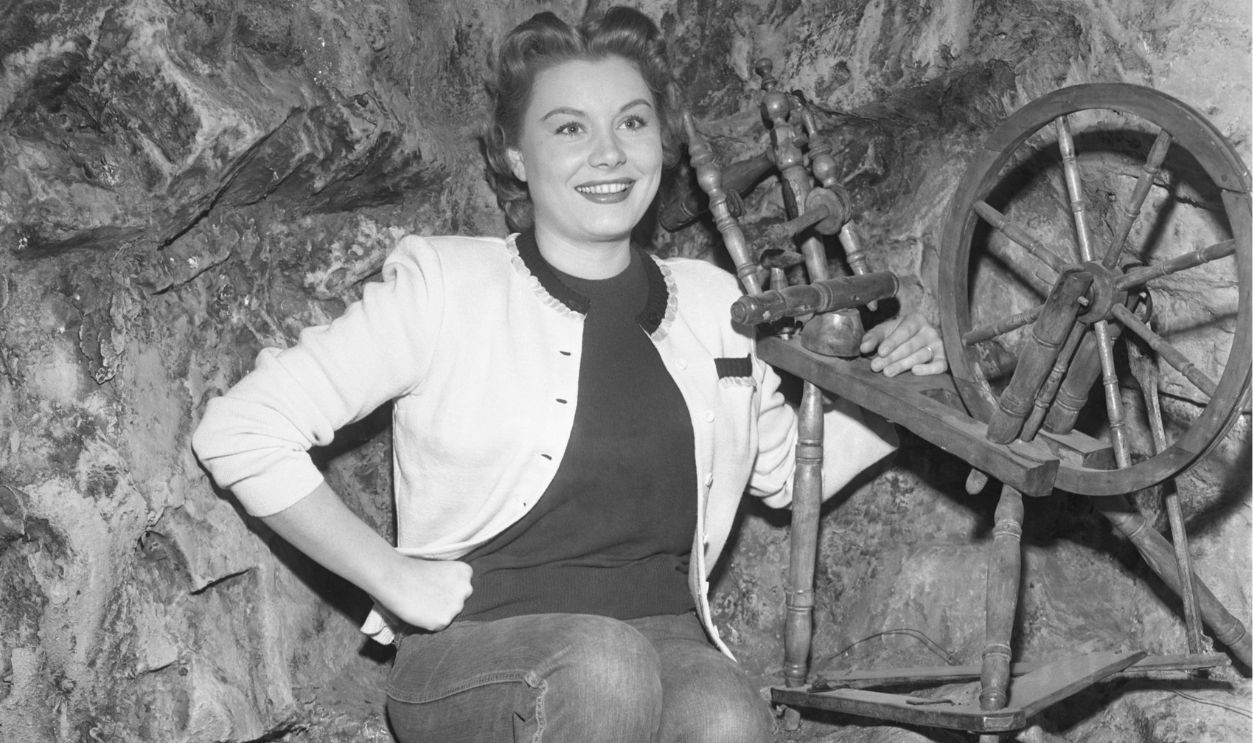 The new demure Barbara Payton poses by a spinning wheel on the set on her new movie in which the actress is starred in a naïve-type role. Miss Payton says she is ‘going to try and forget the past' and concentrate on her career.