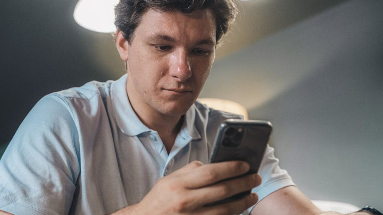 Adult man in casual attire intently using a smartphone indoors, focused and engaged