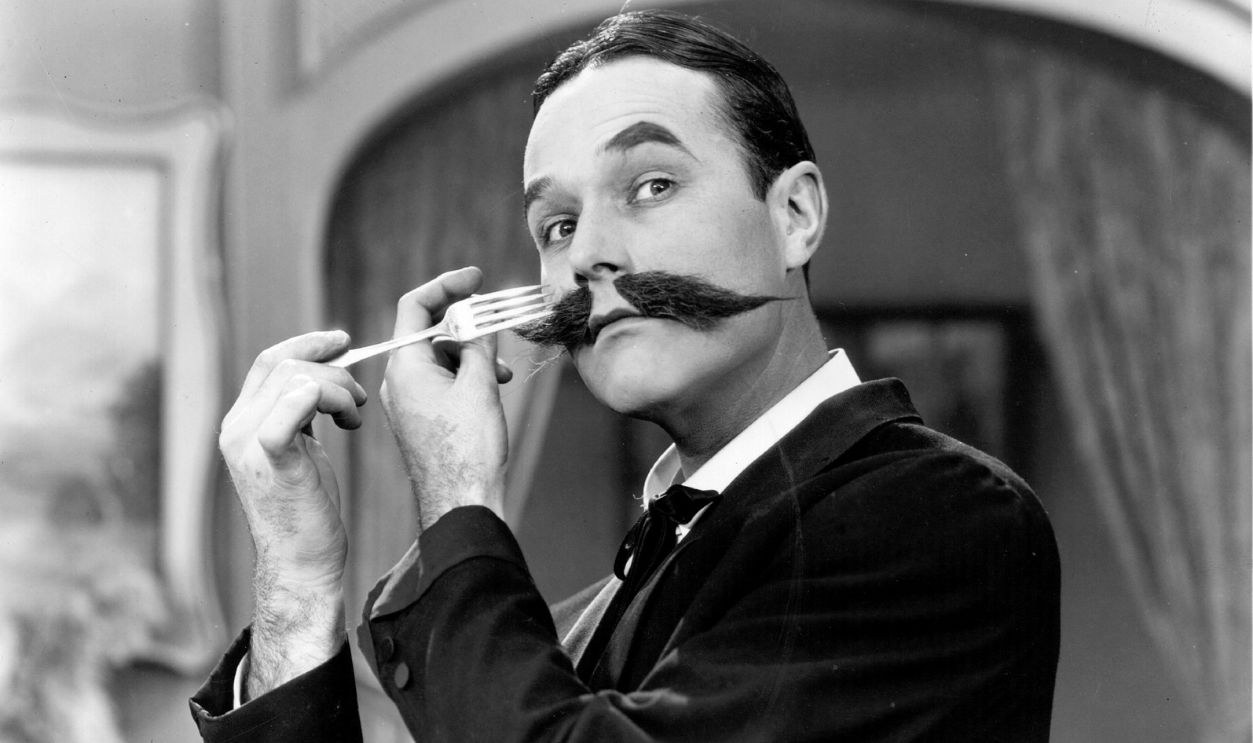 William Haines (1900 - 1973), the American leading man, combs his moustache with the prongs of a fork in a scene from 'Show People', directed by King Vidor for MGM.
