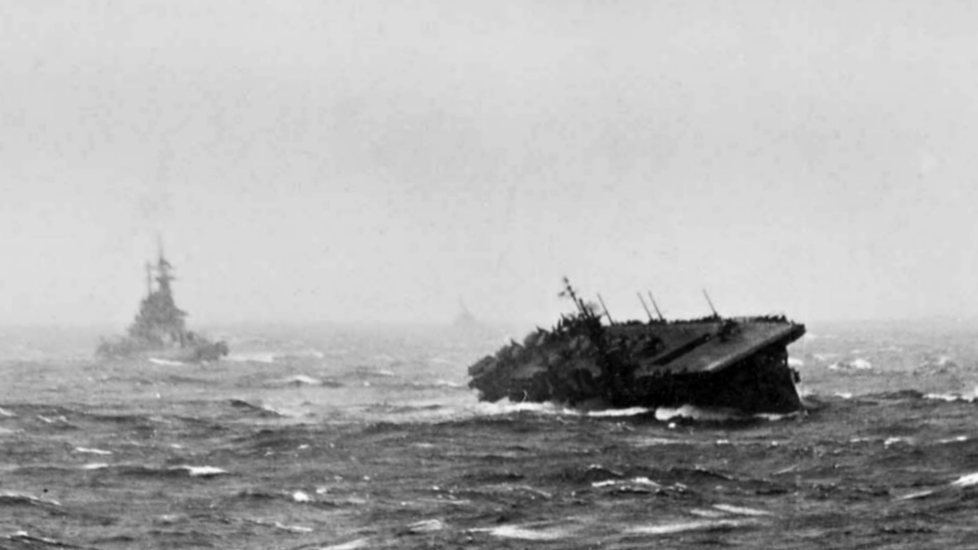 The U.S. Navy light aircraft carrier USS Langley (CVL-27) rolling heavily during Typhoon Cobra, 18 December 1944. A battleship is steaming behind the carrier.