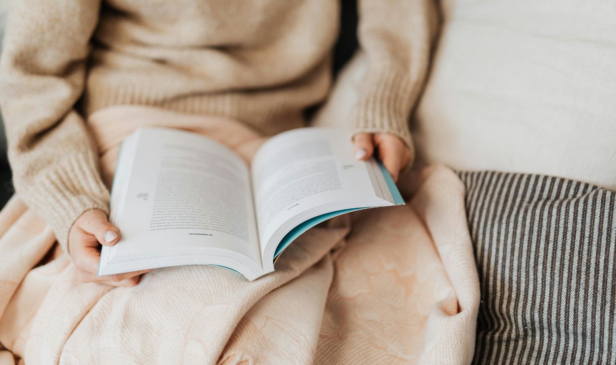 Close-up of hands holding an open book on a cozy blanket indoors