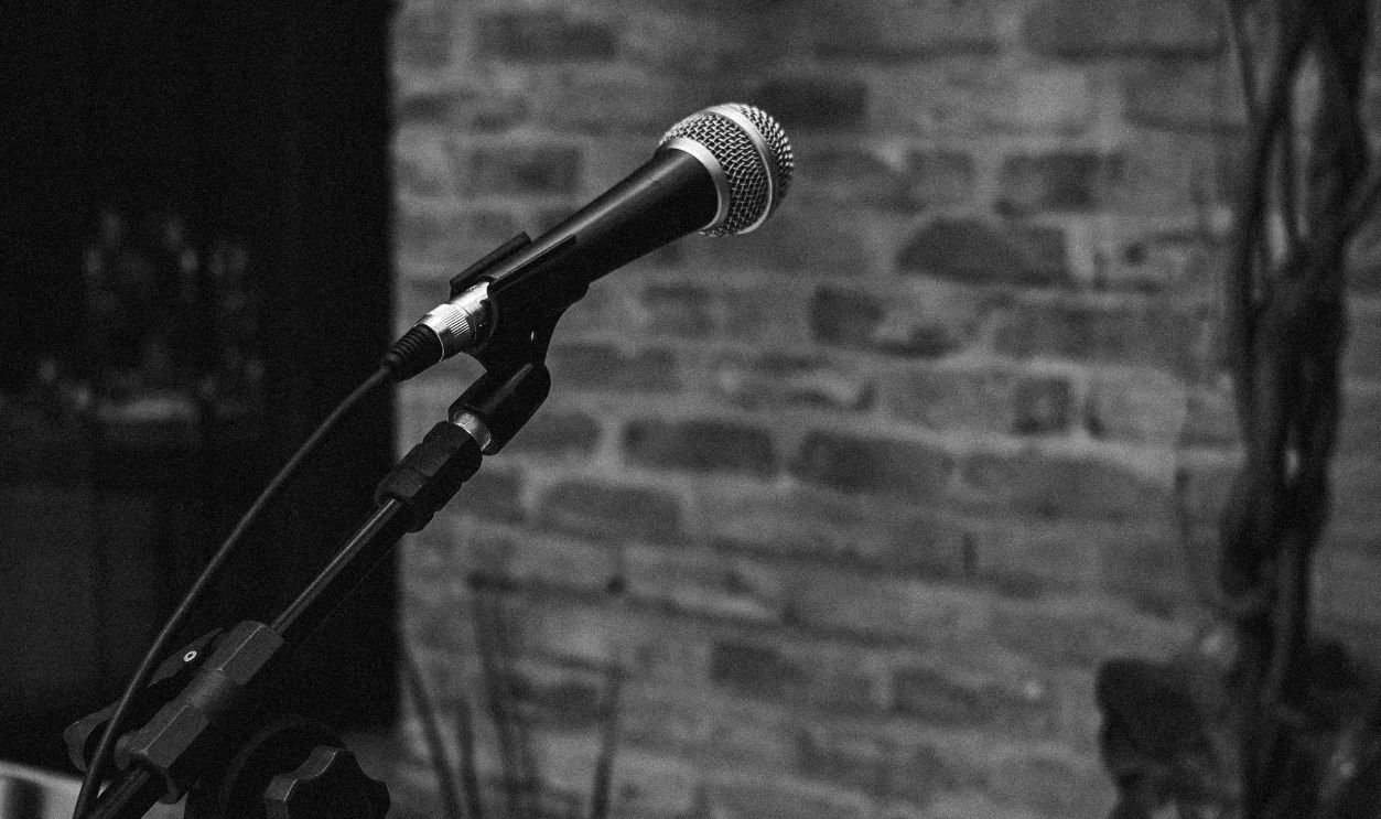 Monochrome image of a microphone stand setup indoors with brick wall backdrop.