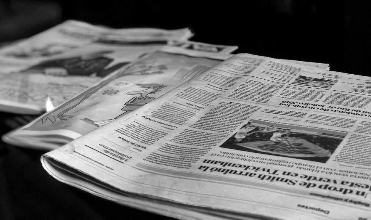 Black and white close-up image of newspapers laid on a table, emphasizing print media.