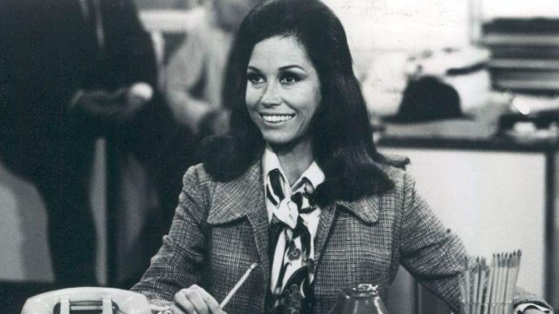 Photo scene from the television program The Mary Tyler Moore Show of Mary Tyler Moore (Mary Richards) at her desk in the WJM-TV newsroom. *Note - this came from a press release dated 1977. The scene is from a 1970 episode.*