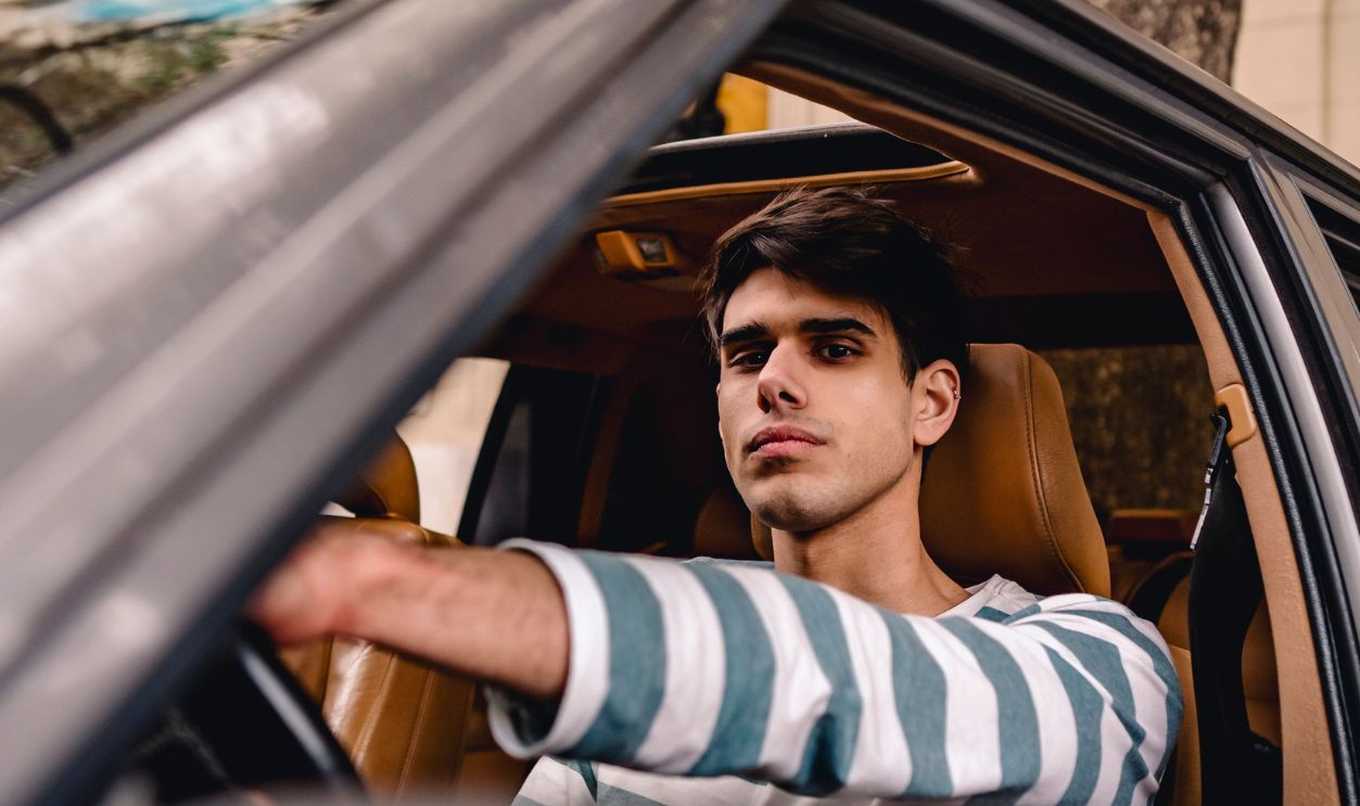 A young man with short brown hair confidently driving a car