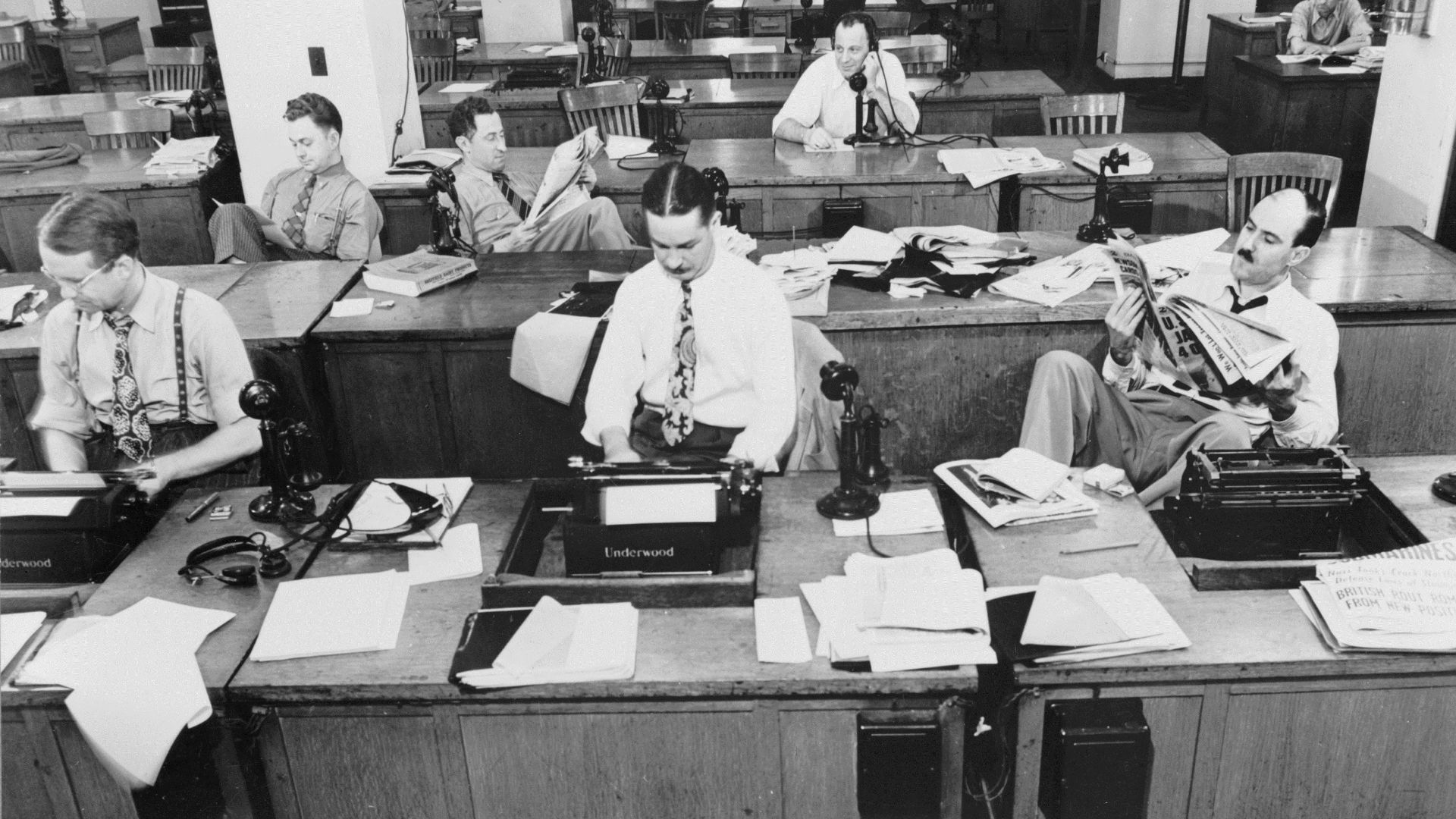 New York, New York. Newsroom of the New York Times newspaper. Reporters and rewrite men writing stories, and waiting to be sent out. Rewrite man in background gets the story on the phone from reporter outside.