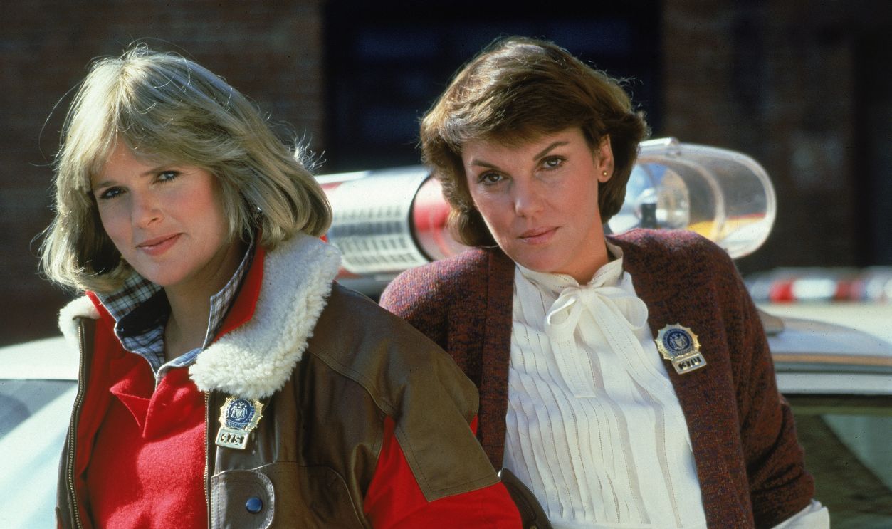 Sharon Gless & Tyne Daly For 'Cagney & Lacey' Actors Sharon Gless (L) and Tyne Daly, both wearing police badges, lean against a police car in a promotional portrait for the television series, 'Cagney & Lacey,' c. 1982.