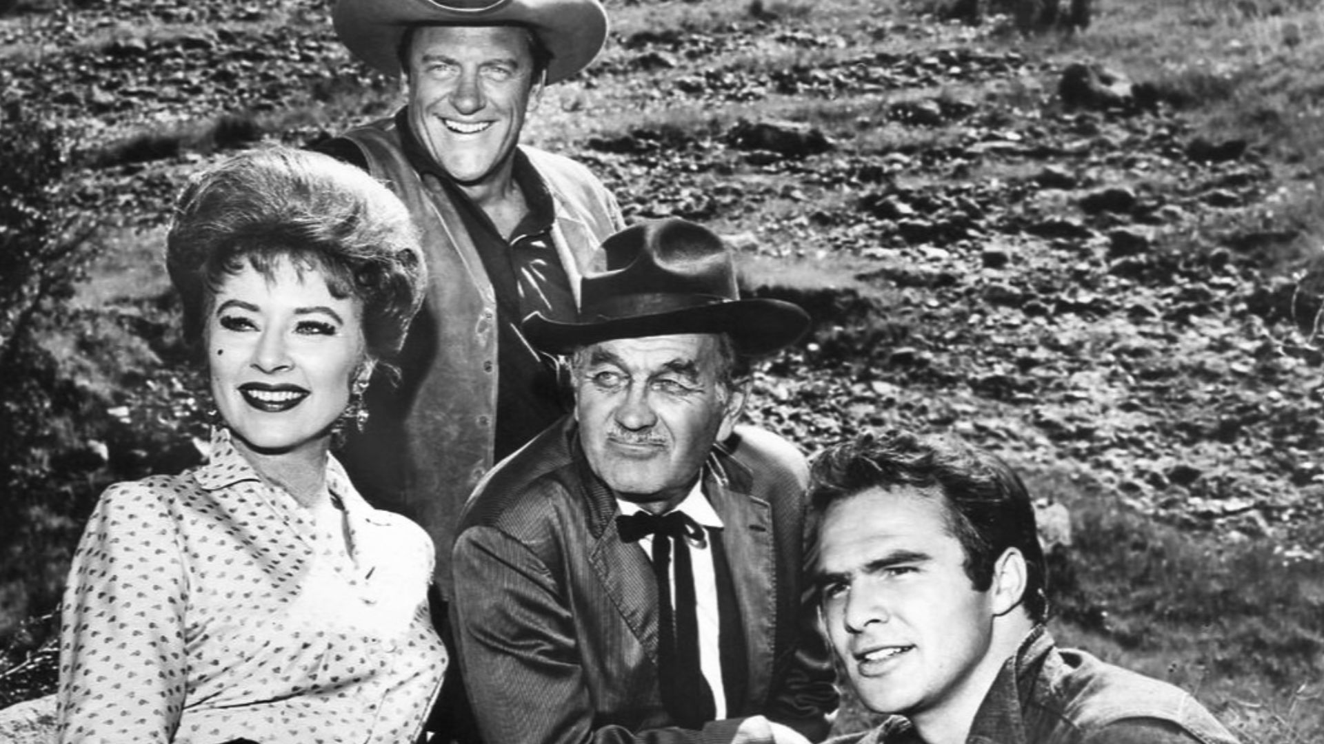 Photo of the main cast for the television program Gunsmoke in 1963.  From left: Amanda Blake (Miss Kitty), James Arness (Matt Dillon), Milburn Stone (Doc Adams), and Burt Reynolds (Quint Asper).