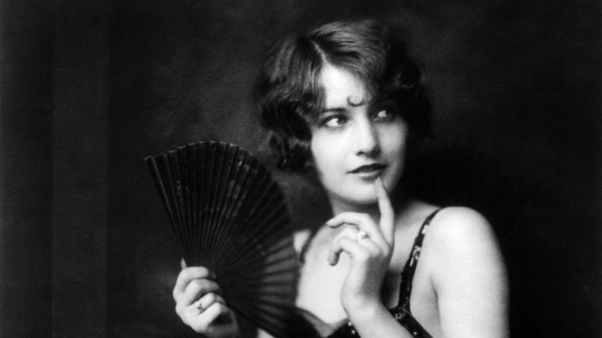 Future Hollywood star Barbara Stanwyck, three-quarter length portrait, seated, turned to the left, holding fan.