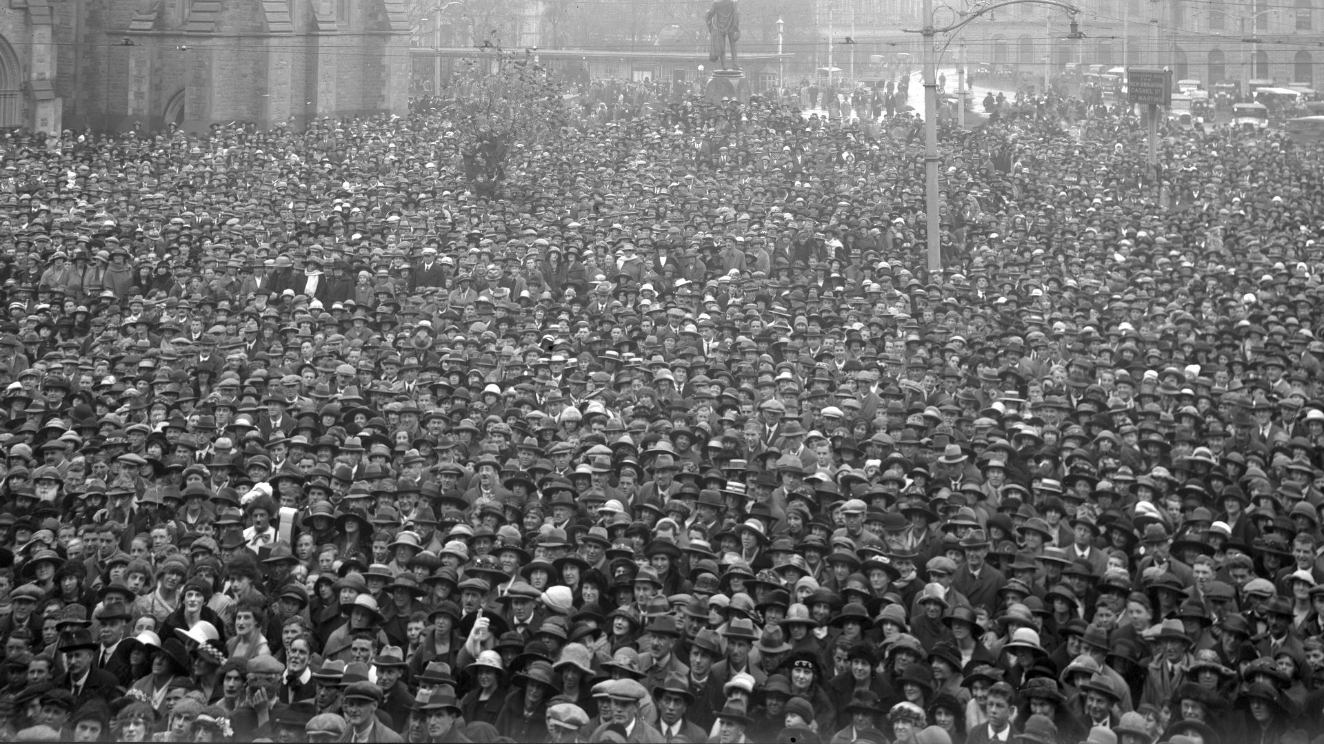 Crowd in Cathedral Square, Christchurch, photographed circa 1920-5 by an unidentified photographer for The Press newspaper. Shows hundreds of faces and hats alongside Christchurch Cathedral. Occasion unidentified. Possibly taken during the announcement of