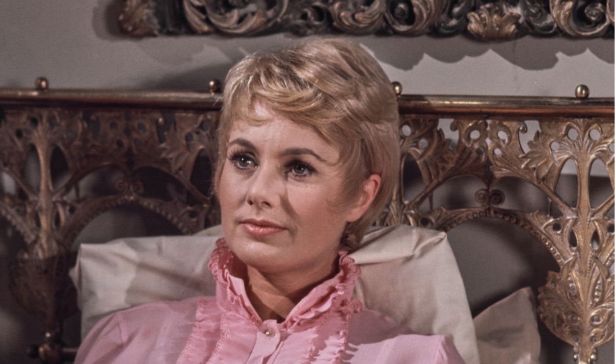 American actress and singer Shirley Jones, wearing a pink nightgown, sitting upright in a bed, against a pillow on a brass headboard, United States, October 1970. 