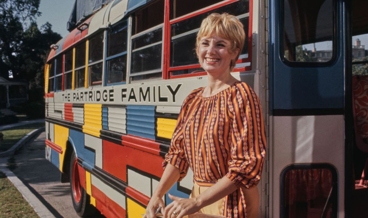 American actress and singer Shirley Jones, wearing an orange-and-black striped outfit with floral motifs, poses beside 'The Partridge Family' bus on the set of the ABC sitcom, United States, August 1971. 