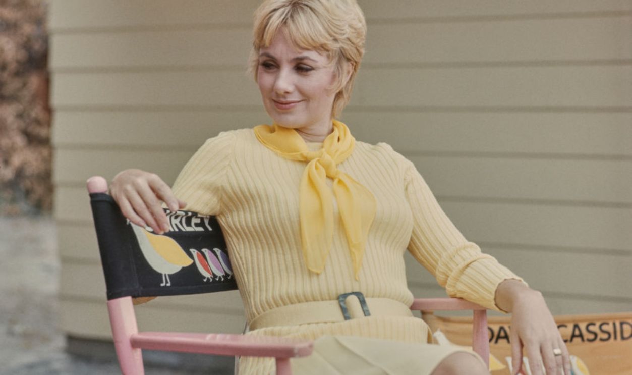 American actress and singer Shirley Jones, wearing a ribbed pale yellow sweater and a yellow neckerchief sits on a folding chair, on 'The Partridge Family' set, United States, August 1971.