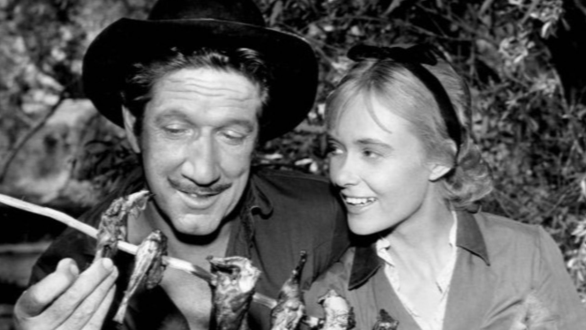Photo of Richard Boone as Paladin and guest star Christine White from the television program Have Gun – Will Travel.  The two cook over a campfire as they plan how to outwit a corrupt sheriff and his family.