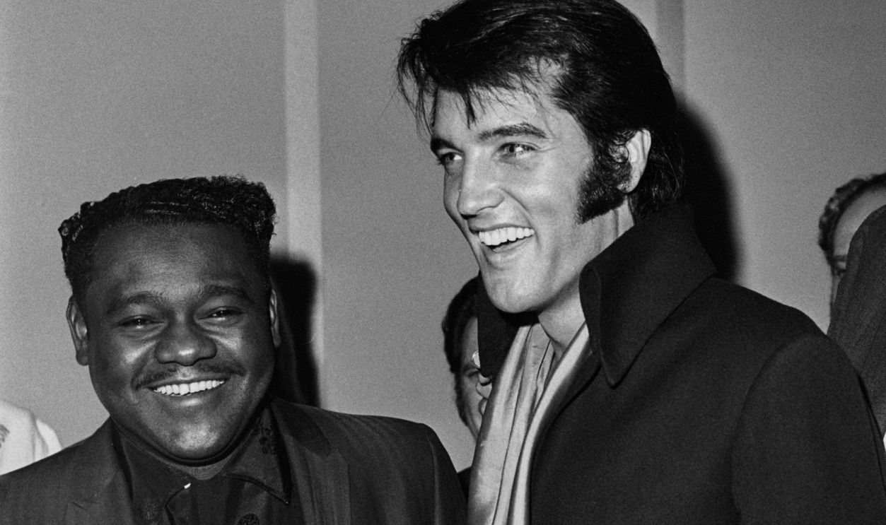 American singer-songwriter and pianist Fats Domino (1928-2017), American singer and actor Elvis Presley (1935-1977), wearing a black jacket with a red-and-black scarf, and a man carrying a camera attend a press conference, held in the 'convention hall' of the International Hotel in Las Vegas, Nevada, 1st August 1969. The press conference was convened after Presley's first live performance in eight years, also at the International Hotel. 