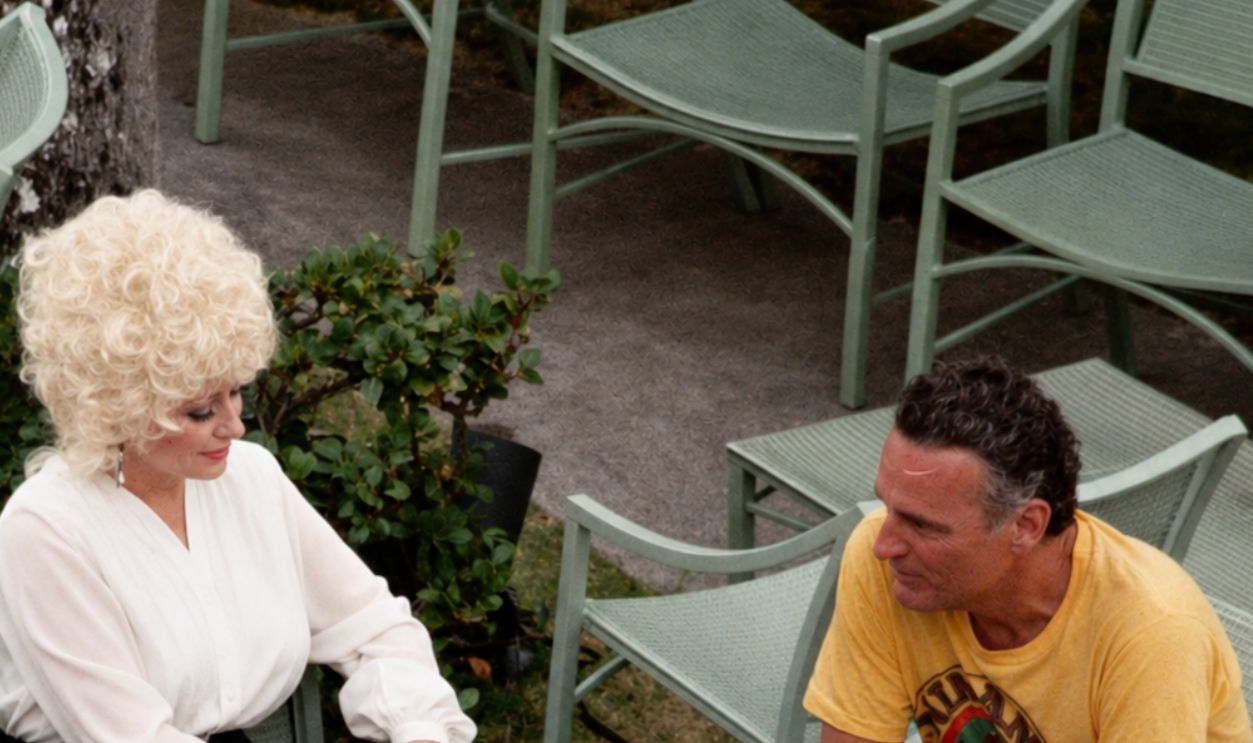 Dolly Parton relaxing around the pool area of the Kahala Hilton Hotel, May 1984, with her husband Carl Dean next to her, in the yellow shirt.