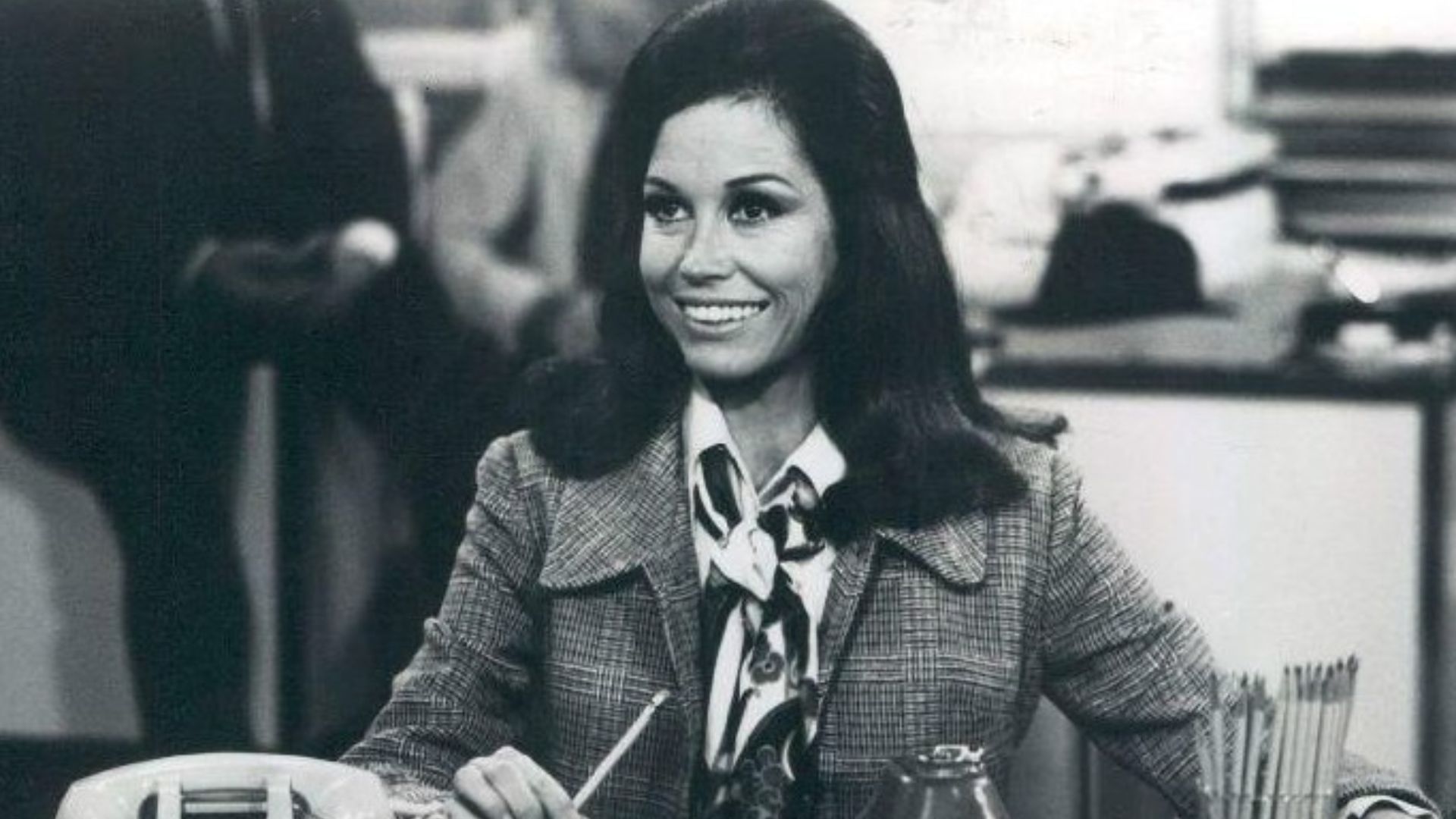 Photo scene from the television program The Mary Tyler Moore Show of Mary Tyler Moore (Mary Richards) at her desk in the WJM-TV newsroom. *Note - this came from a press release dated 1977. The scene is from a 1970 episode.*