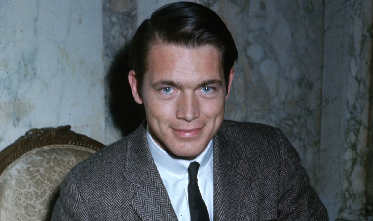 American actor Chad Everett smiles while sitting in a front of a marble wall