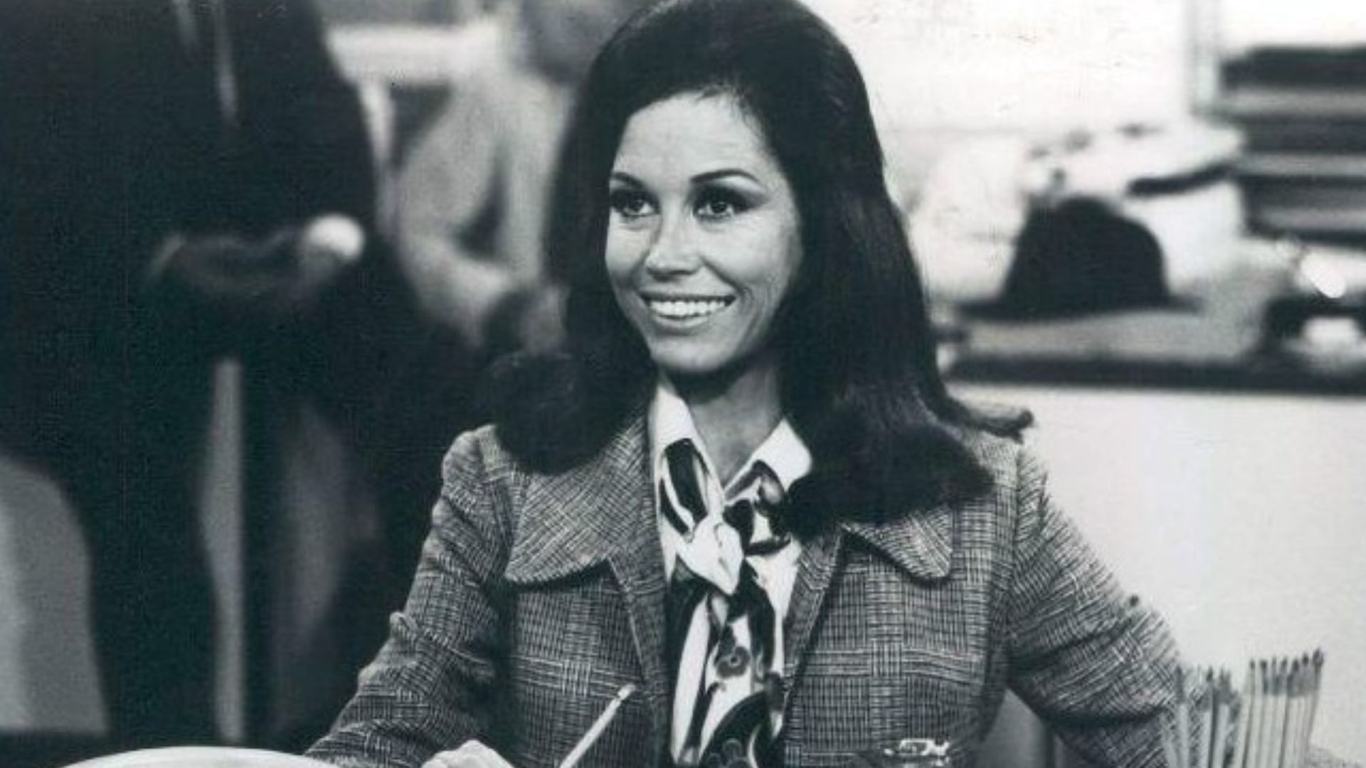 Photo scene from the television program The Mary Tyler Moore Show of Mary Tyler Moore (Mary Richards) at her desk in the WJM-TV newsroom. *Note - this came from a press release dated 1977. The scene is from a 1970 episode.*