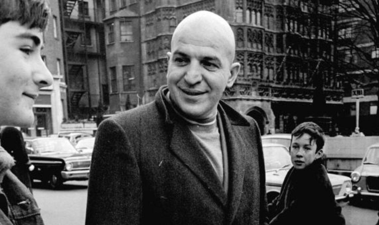 Actor Telly Savalas surrounded by young fans on bikes, during a walk in London with his wife, Marilynn Gardner. February 1968.