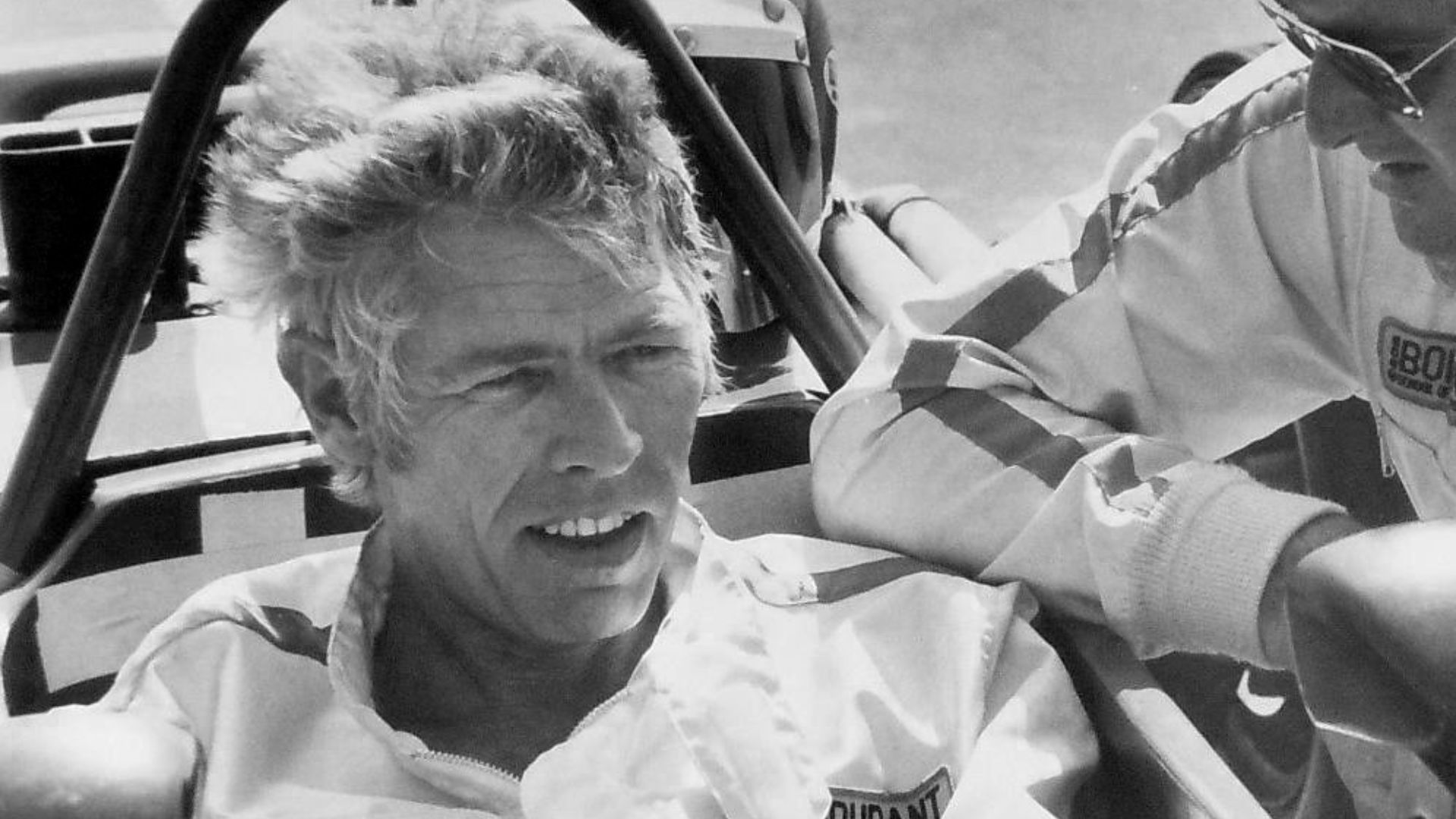 Photo of Bob Bondurant teaching actor James Coburn how to drive a race car.