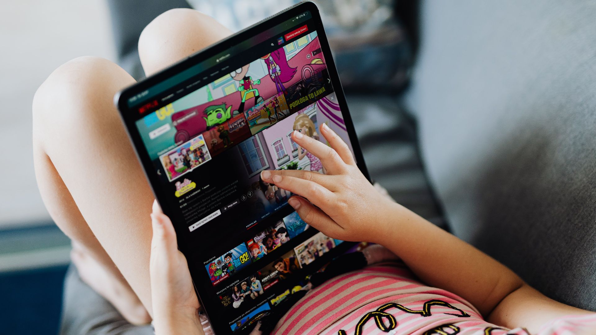 A child using a tablet for streaming cartoons, relaxing on a couch indoors.