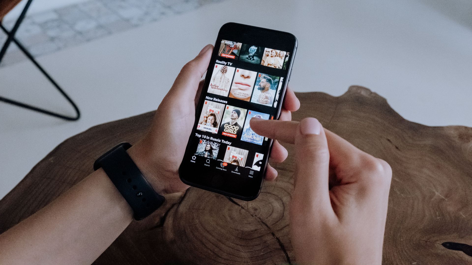 A person using a smartphone to explore and select shows on a streaming platform indoors.
