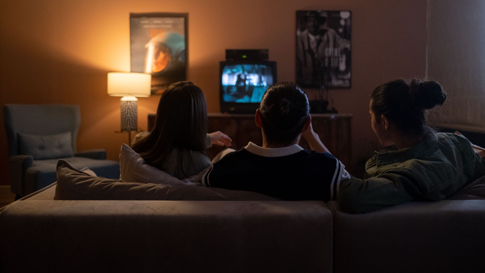 Three people enjoying a relaxed movie night at home, sitting on a couch in a cozy living room.