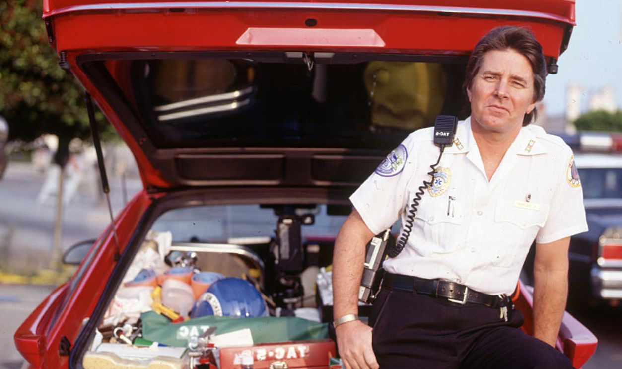 Musician Bobby Sherman, dressed as a paramedic, stands near an emergency vehicle.