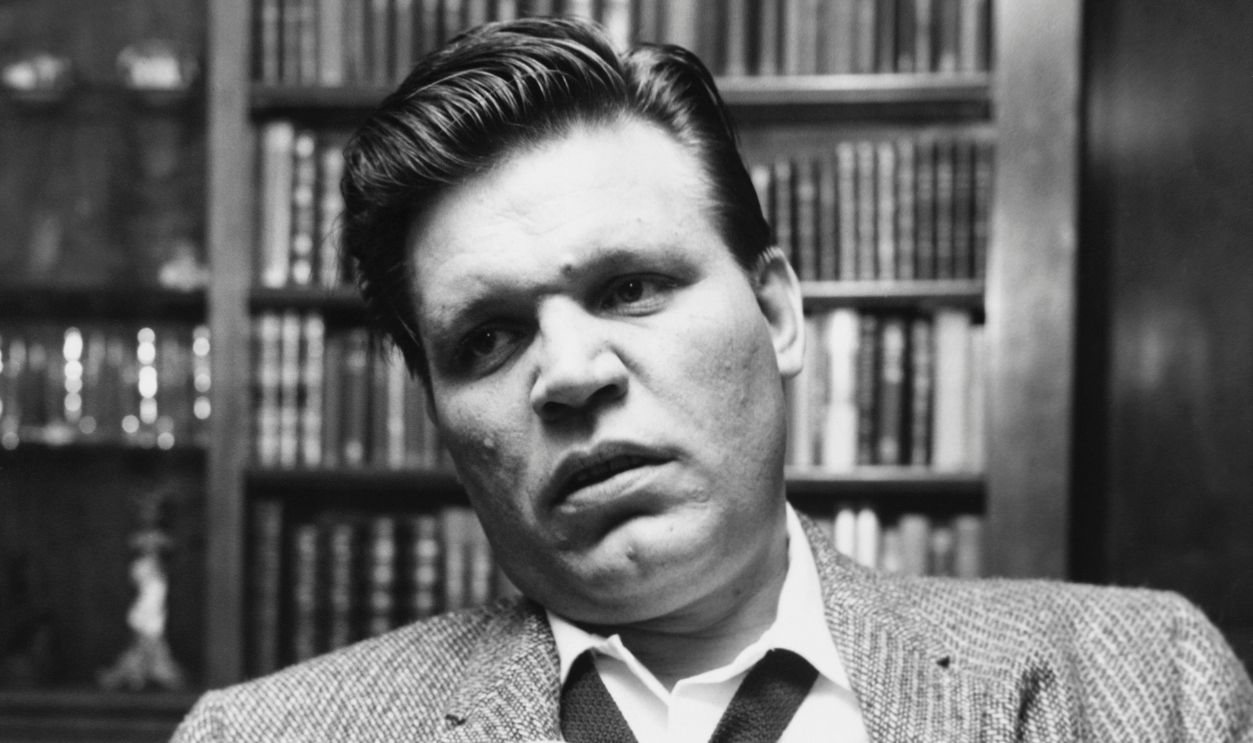 Actor Neville Brand holds the lapel of his suit jacket. 