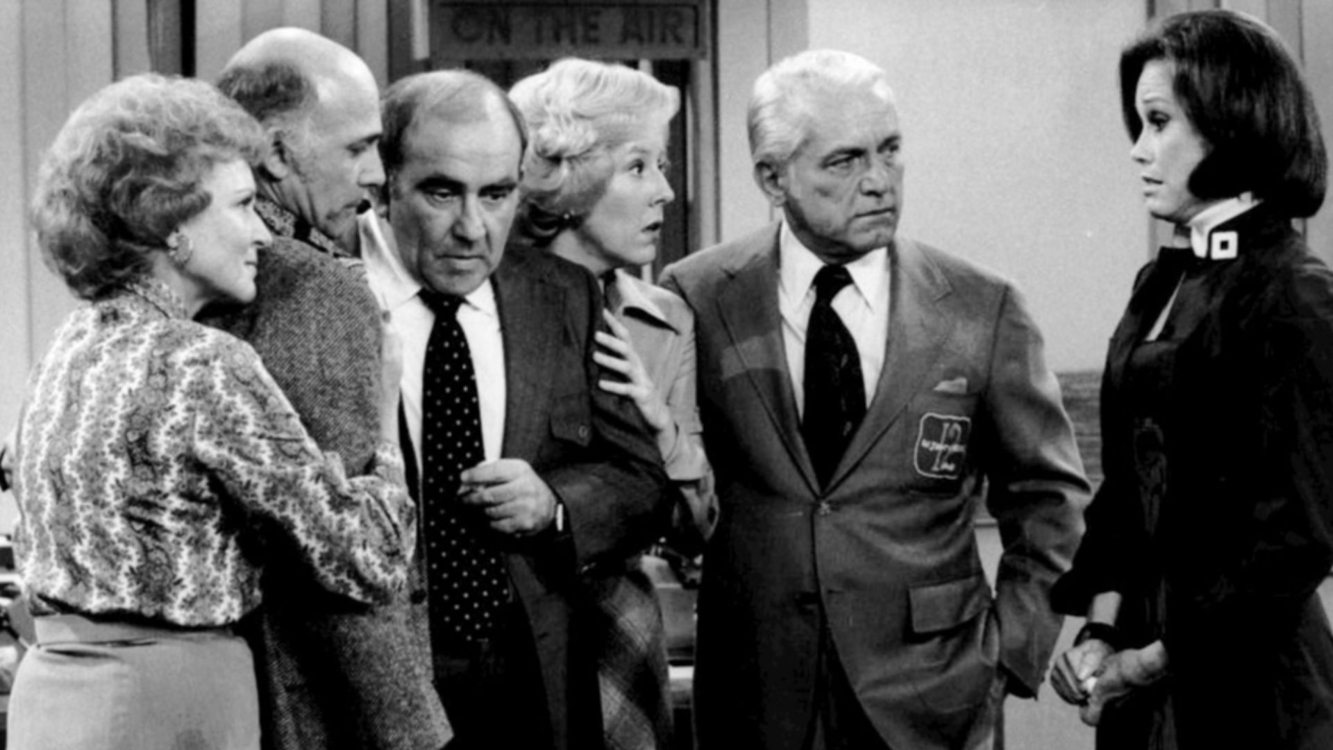 Cast photo from the television program The Mary Tyler Moore Show.  After the news that most of the WJM-TV staff has been fired, everyone gathers in the newsroom.  From left-Betty White (Sue Ann Nivens), Gavin MacLeod (Murray Slaughter), Ed Asner (Lou Gran