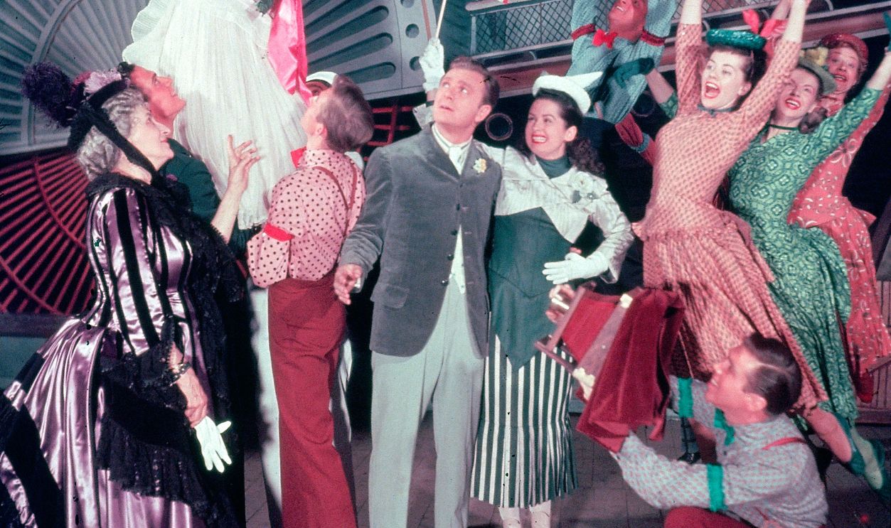 Canadian actress Allyn McLerie raises her arm while others, including American actors Eddie Albert (center) and Mary McCarty ( 1923 - 1980) (center, holding flag) watch, in a scene from the Broadway musical 'Miss Liberty,' at the Imperial Theatre, New York, New York, July 1949.