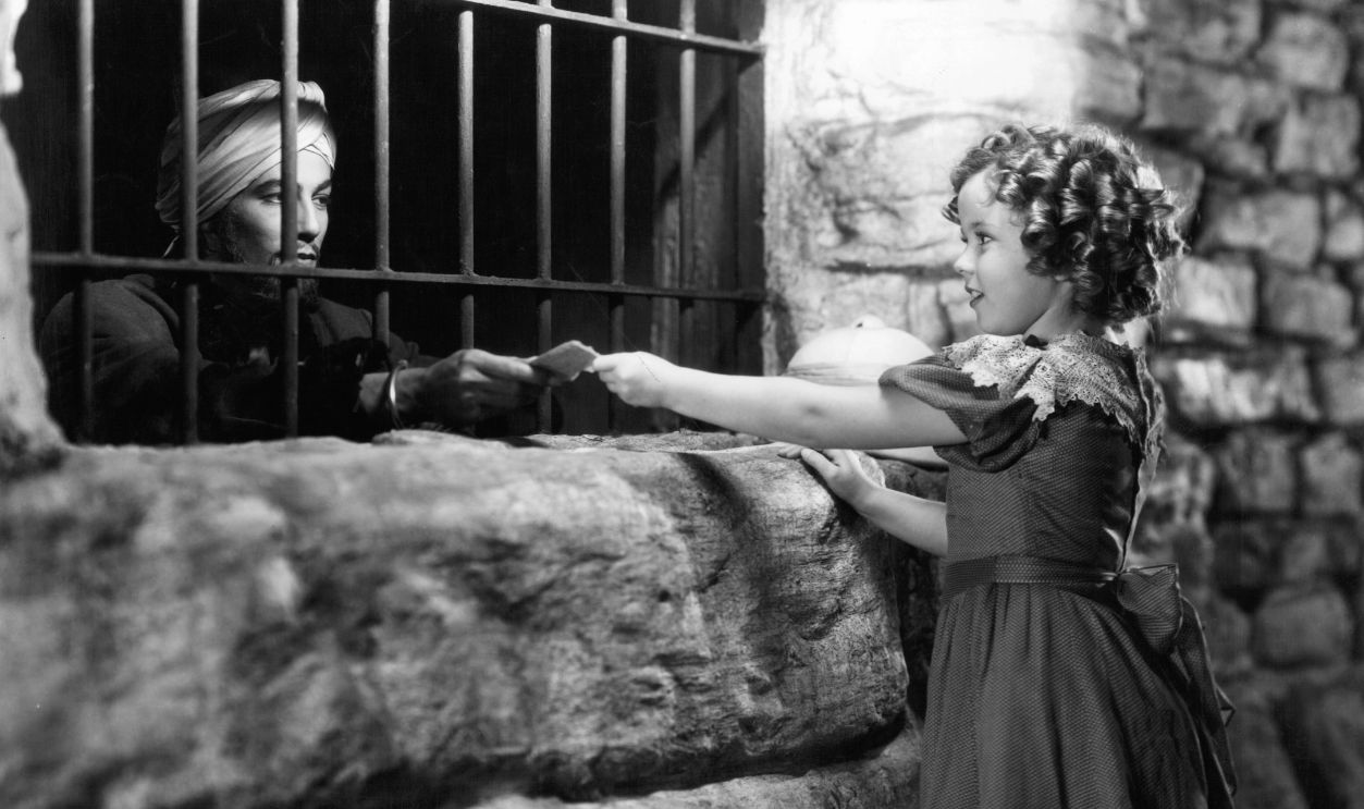 Shirley Temple hands Cesar Romero a letter through the bars of a window in a scene from the film 'Wee Willie Winkie', 1937. 